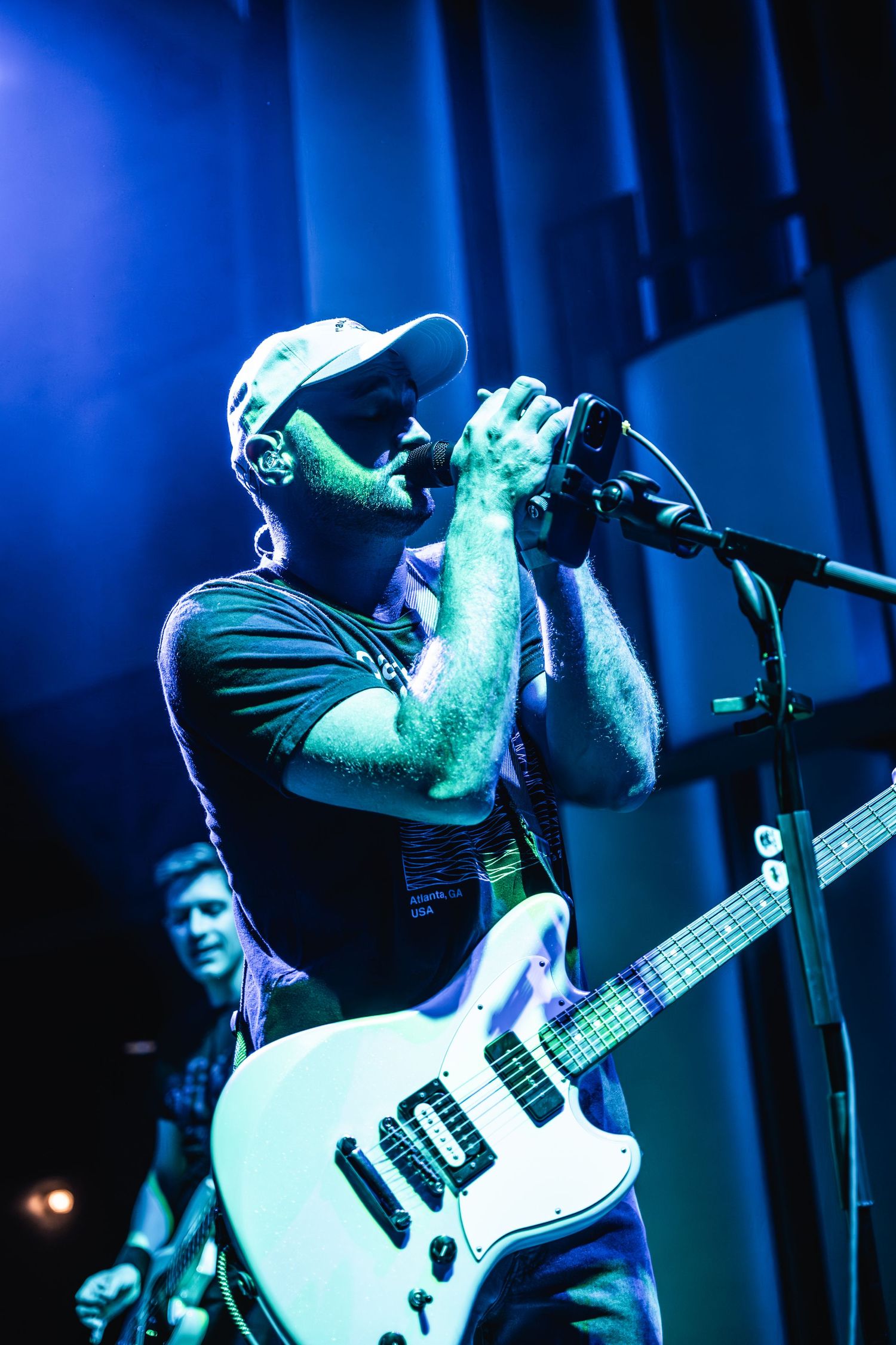 Singer performs passionately on stage with white electric guitar under blue stage lighting.