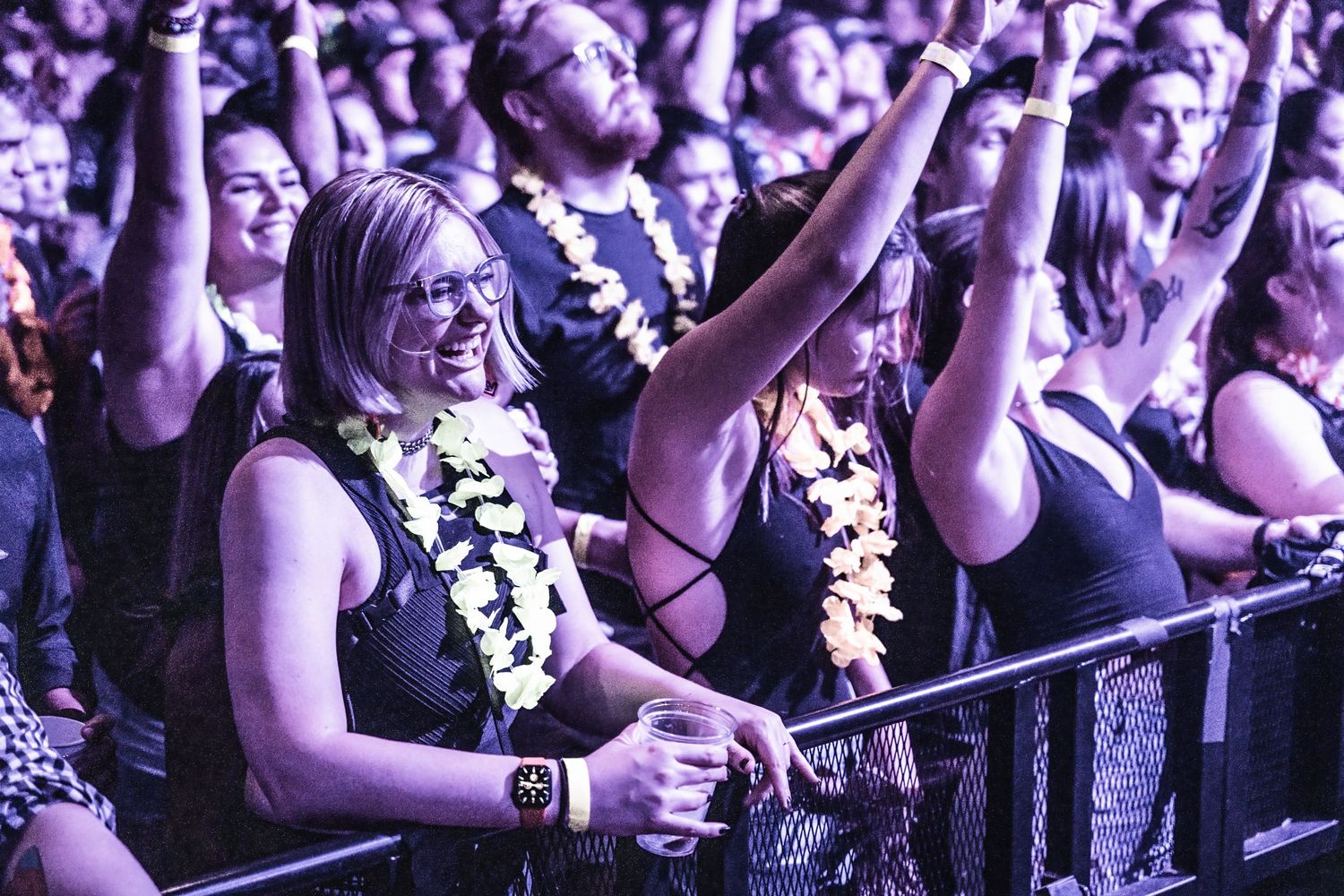 Concert audience members wearing leis cheer and raise hands during performance.