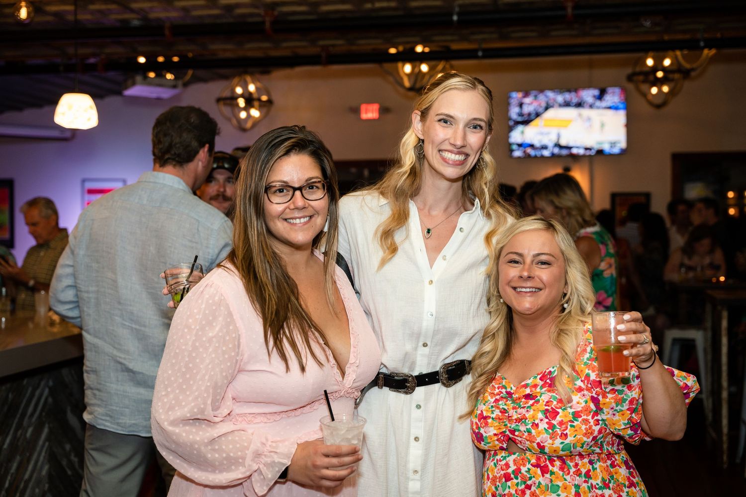 Three friends enjoying drinks and conversation at an indoor social event.