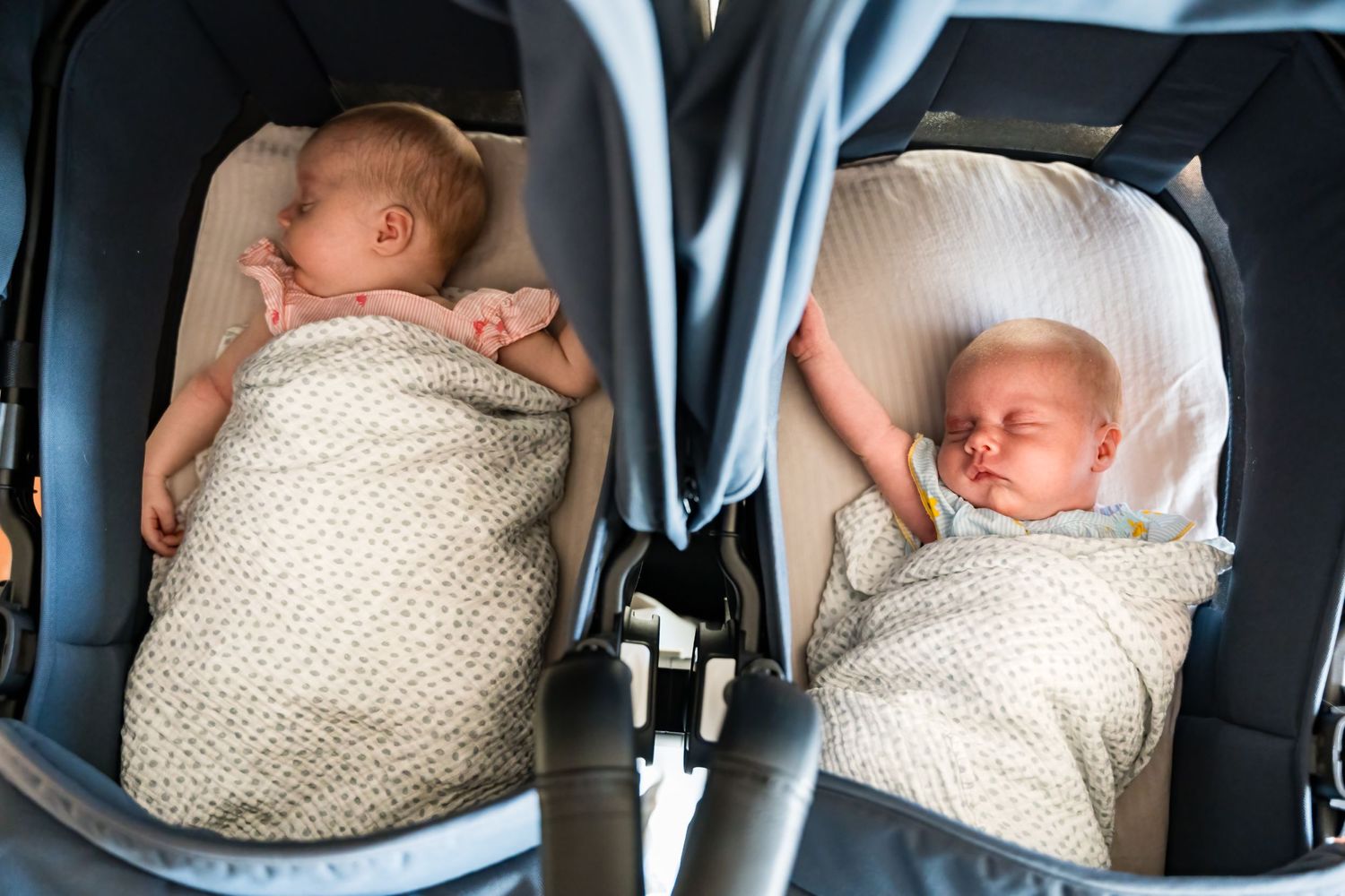Two infants sleeping peacefully in matching car seats with white knit blankets.