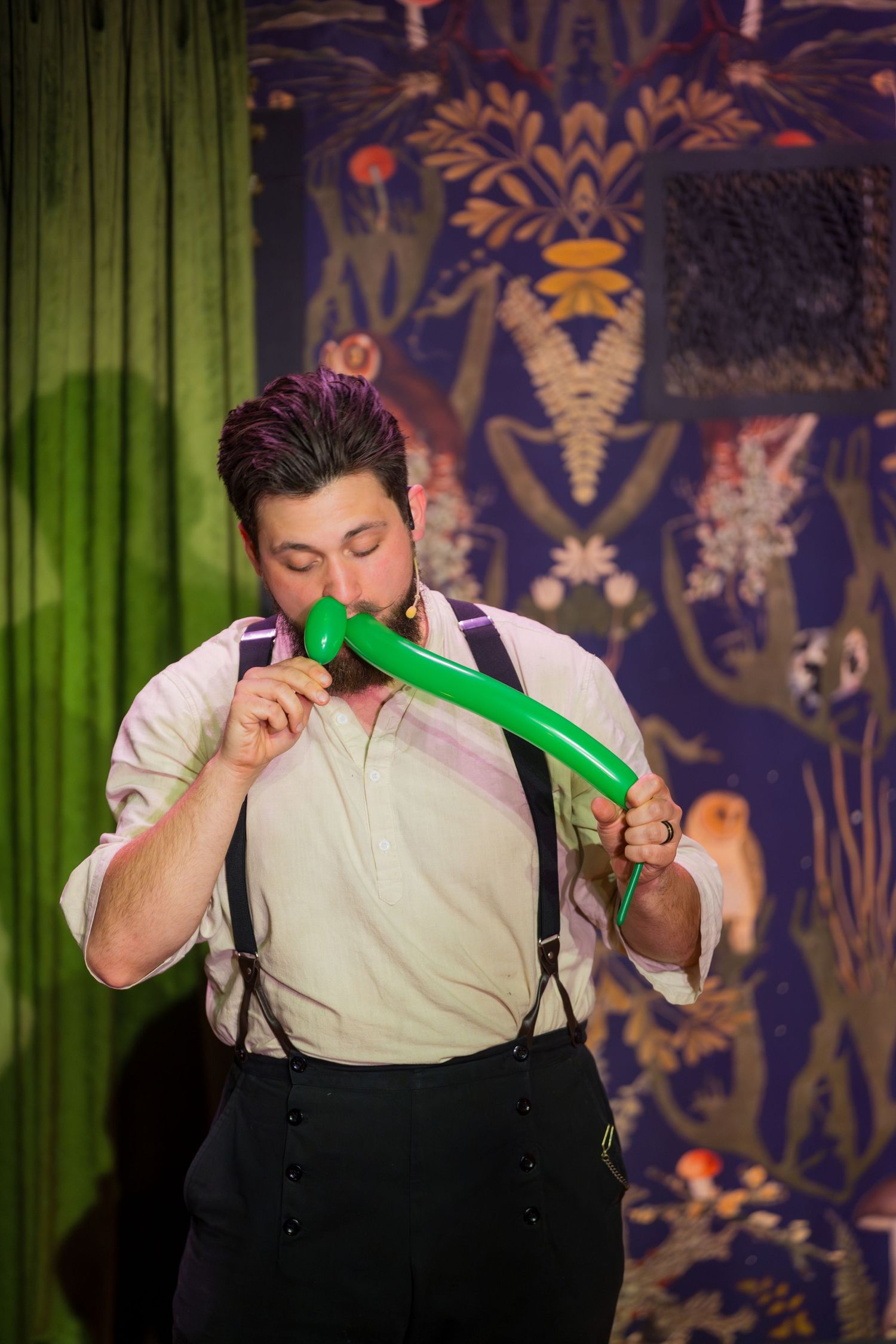 Performer on stage blowing up a green balloon in a sequence of progressive images against a dark patterned backdrop.
