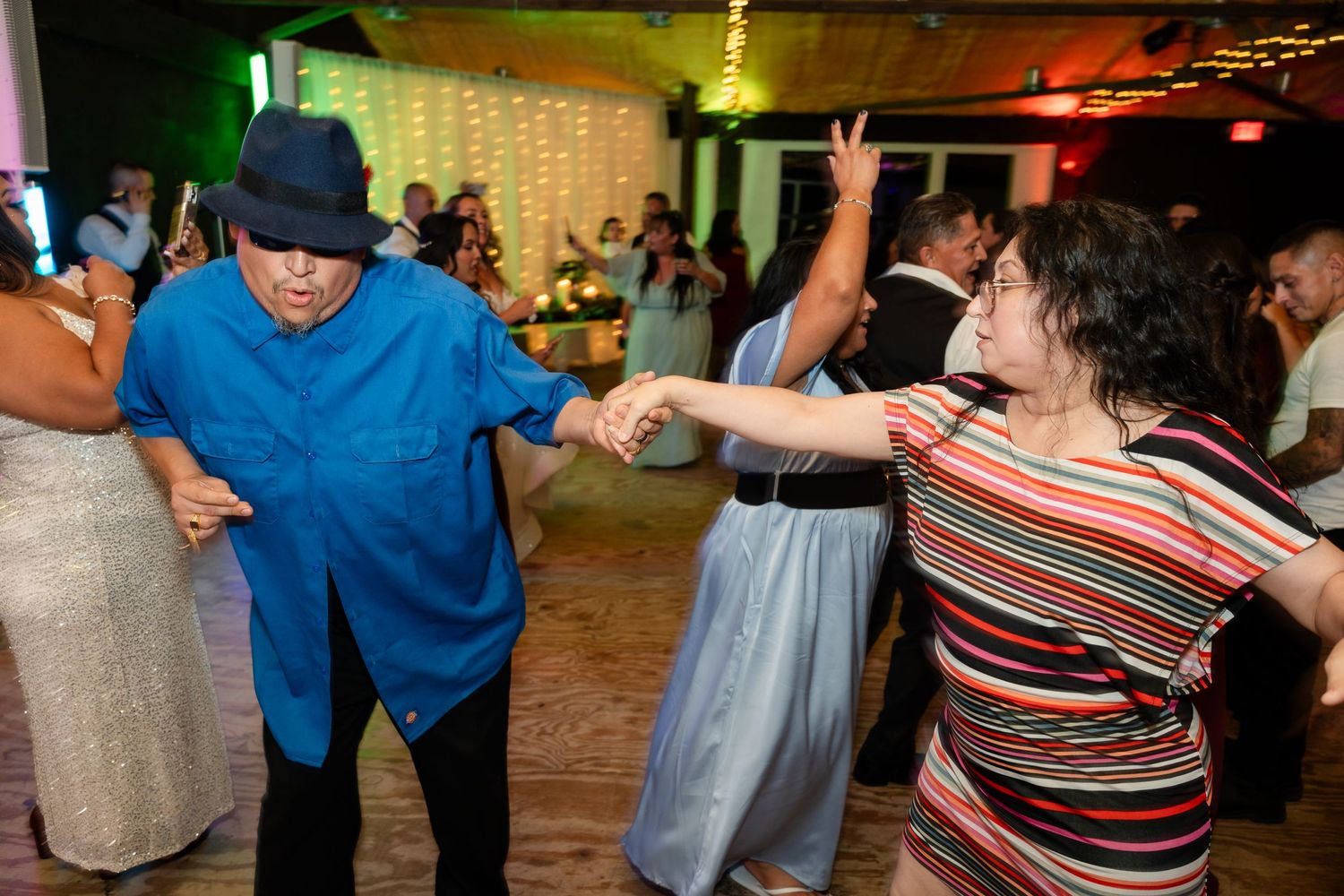 Party guests dancing together at an event with string lights and colorful ambient lighting.