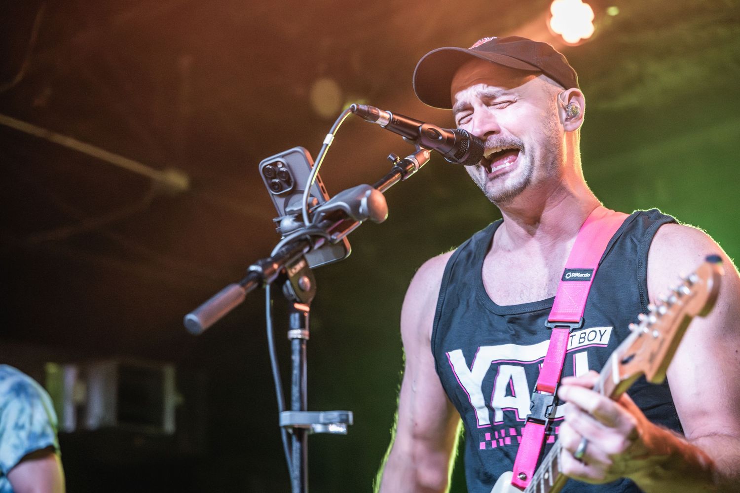 Energetic musician performing with guitar and microphone under colorful stage lights.