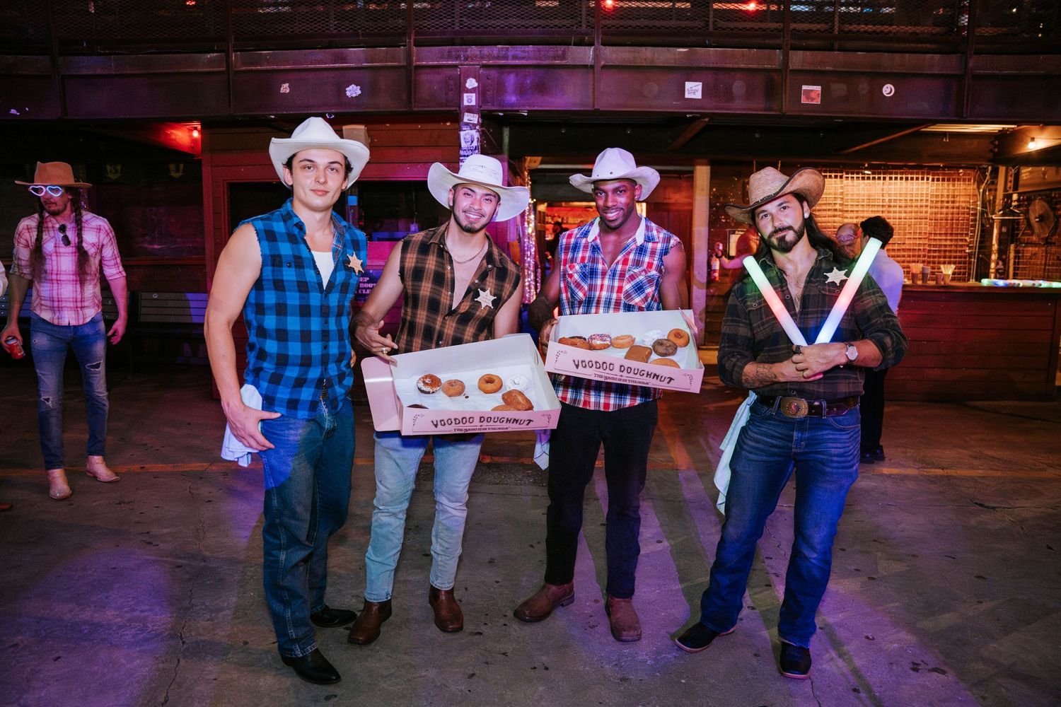 Group dressed in western attire poses with props at indoor venue.
