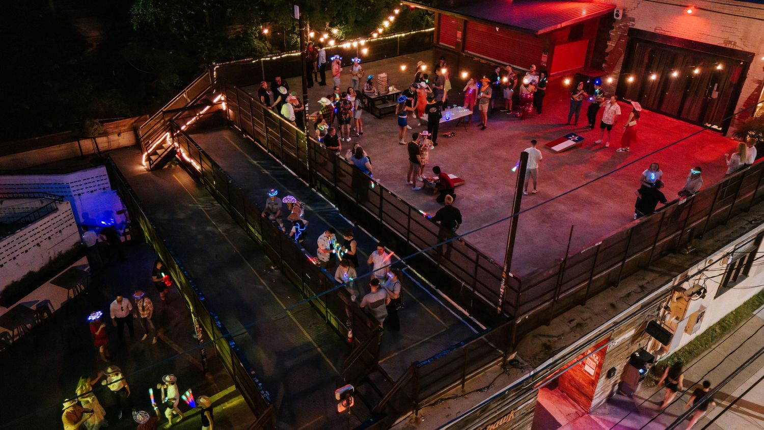 Aerial view of nightclub patio with red lighting and string lights over dancing crowd.