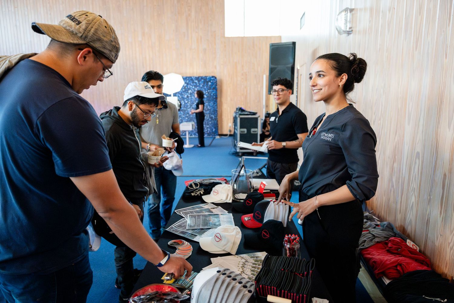 People sorting through clothing and merchandise at a casual indoor event with blue walls.