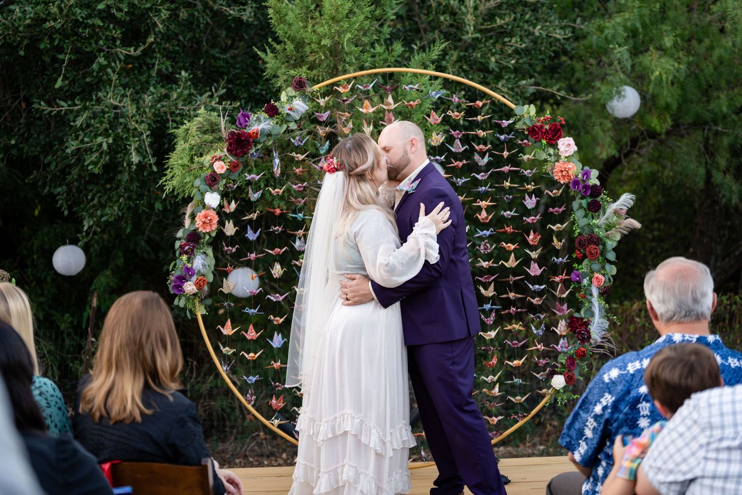 A wedding ceremony moment beneath a golden hoop arch adorned with origami butterflies and flowers.