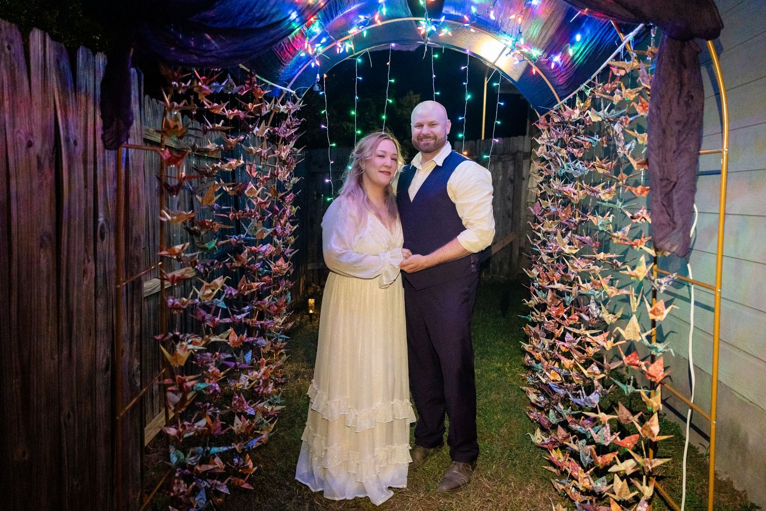 Couple stands under illuminated archway decorated with colorful paper cranes.