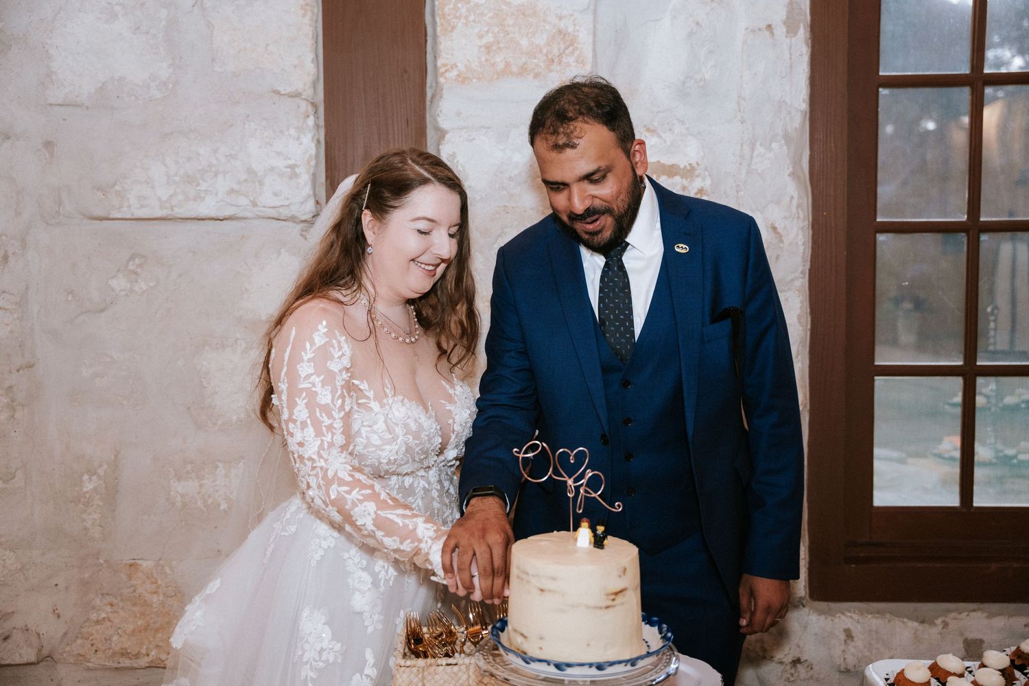 A couple in formal attire cutting their white wedding cake together at their reception.