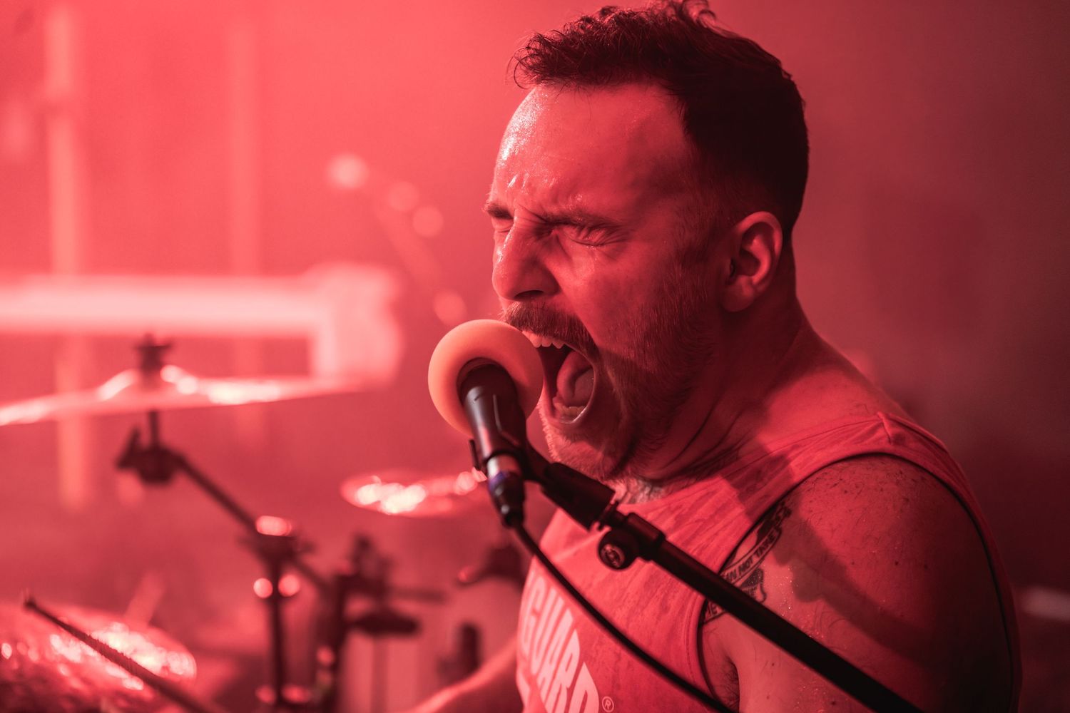 Performer singing intensely on stage bathed in dramatic red lighting.