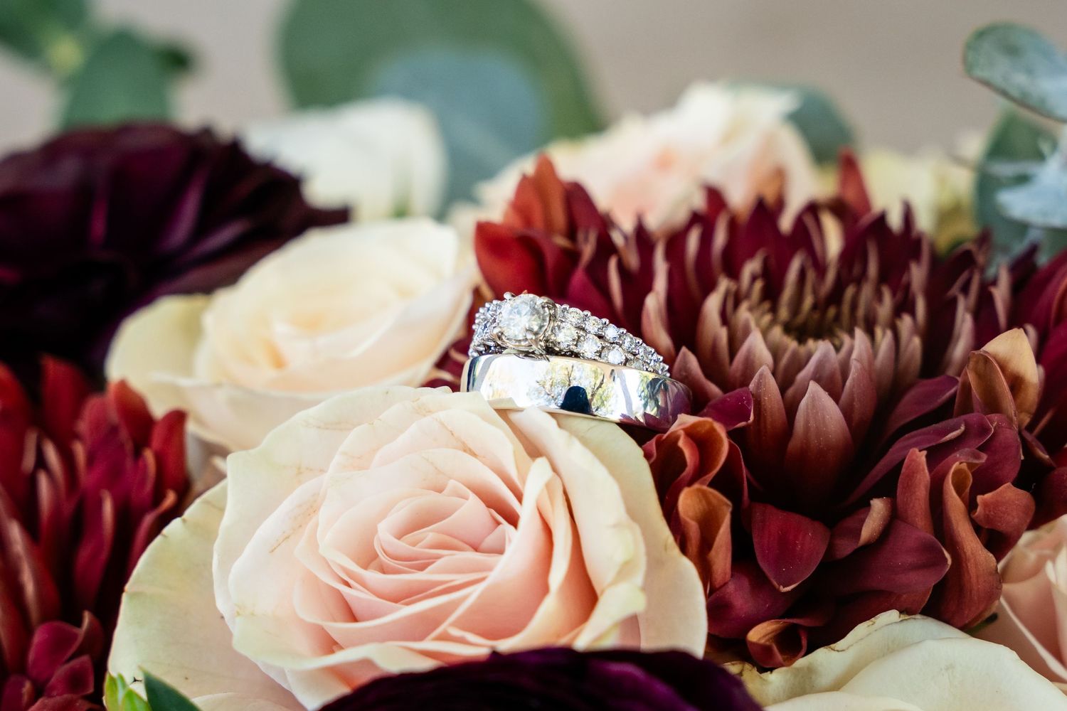 Diamond engagement ring nestled among burgundy and blush roses in a floral arrangement.