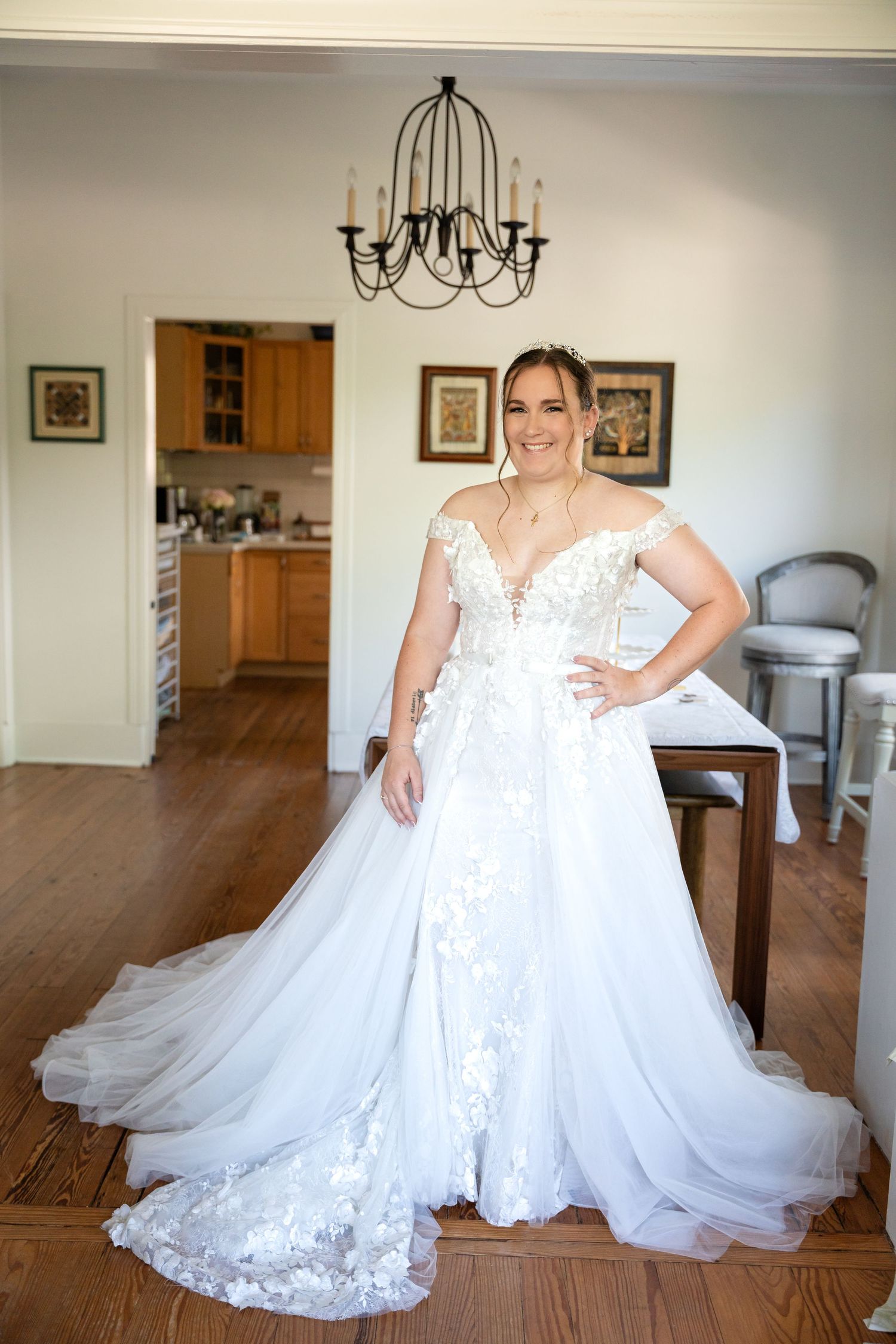 A stunning off-shoulder wedding gown with lace details and long train photographed in a sunlit room.