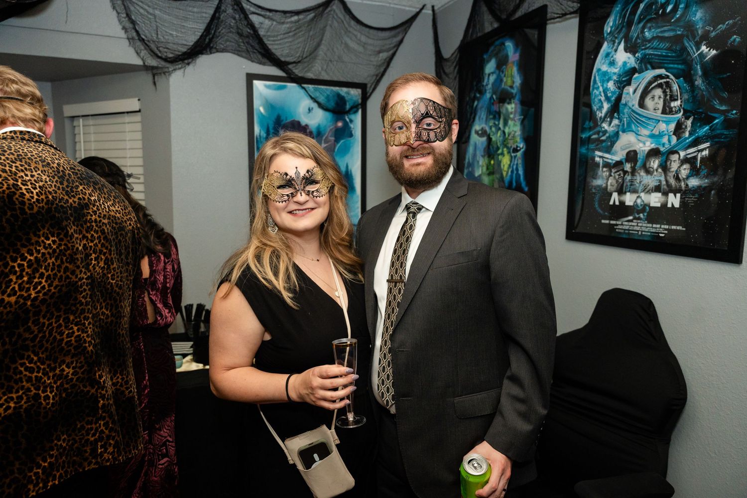 Party guests in festive attire pose in front of wall decorated with movie posters.