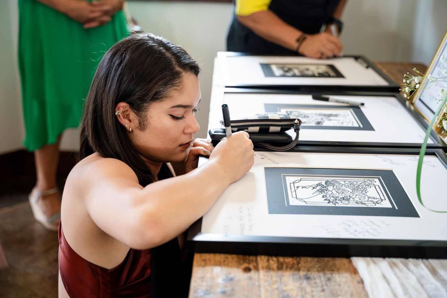 A creative artist works diligently on a detailed ink drawing at a wooden desk.