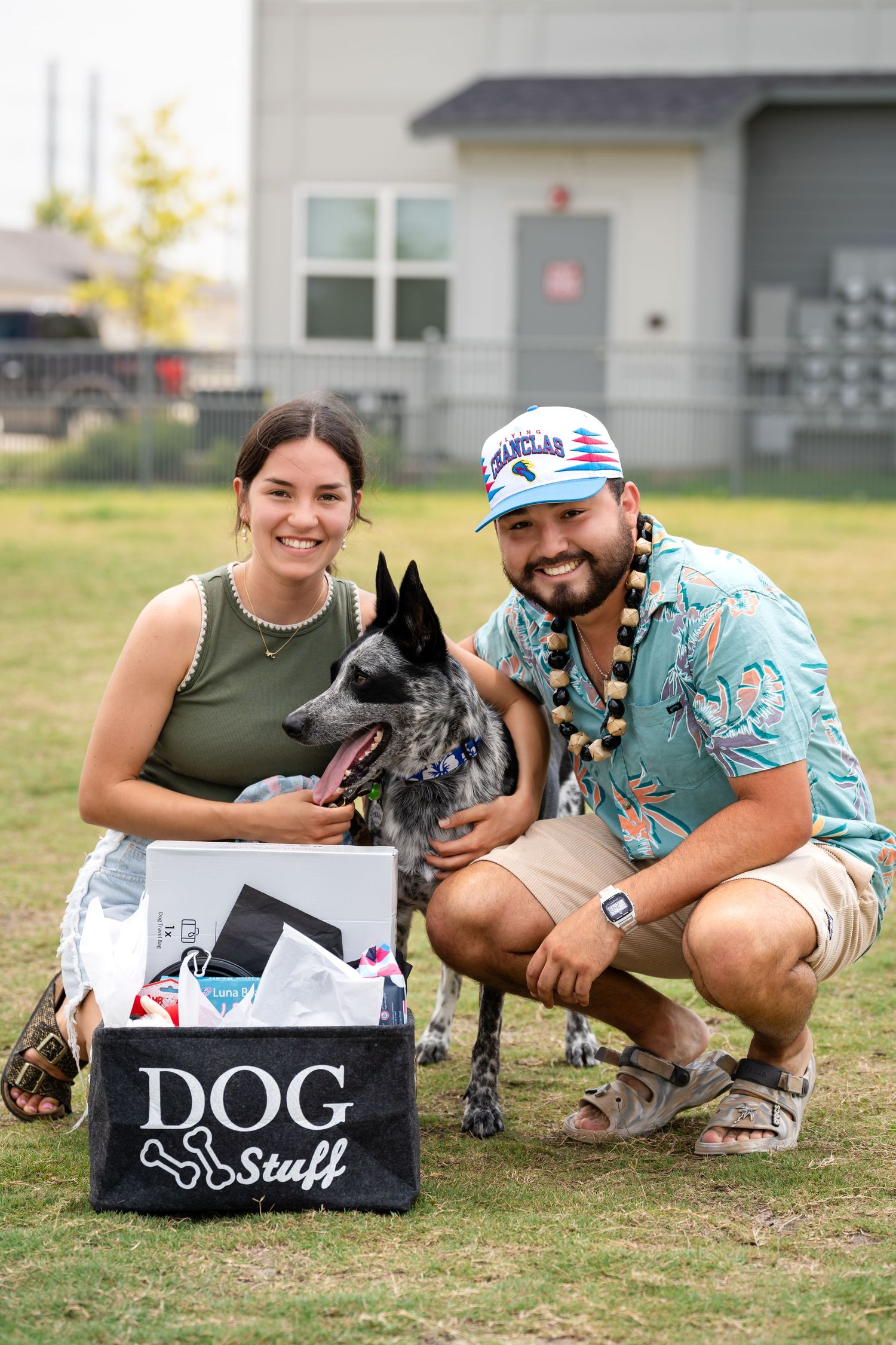 A couple poses with their German Shepherd dog and 'Dog Stuff' box on a grassy lawn.