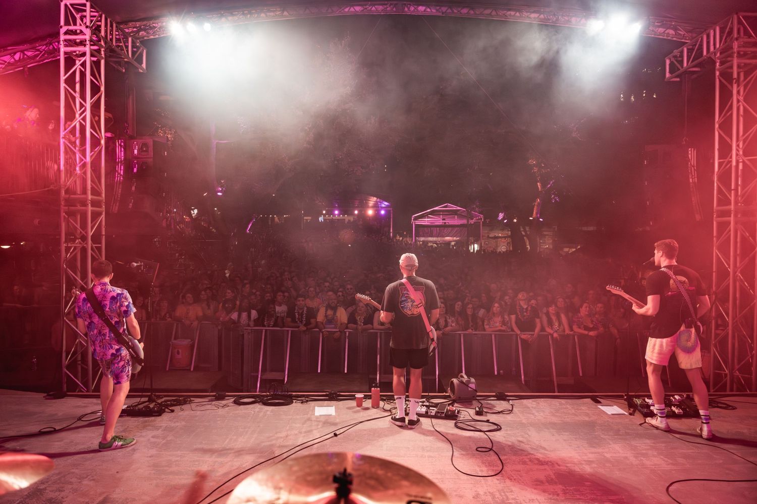 Wide shot of band performing on stage with crowd visible in foreground under red lighting.