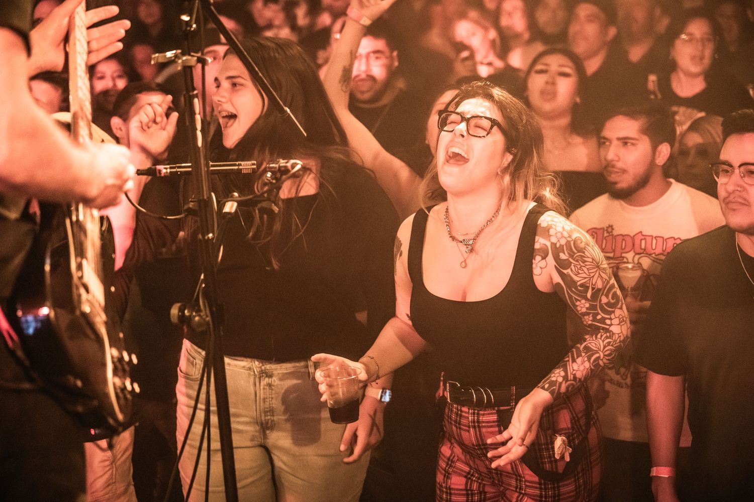 Concert crowd at live show with enthusiastic fan in glasses and black tank top reacting among audience members.