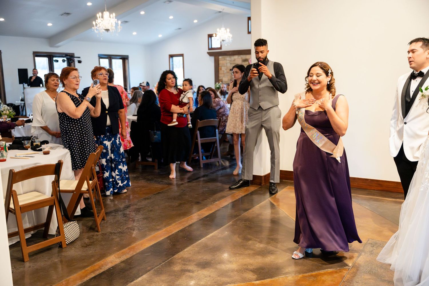 Wedding guests stand and clap during a special moment at an indoor reception venue with polished concrete floors.