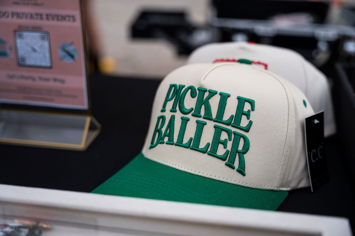 A white and green baseball cap with 'PICKLE BALLER' text displayed on the front panel.