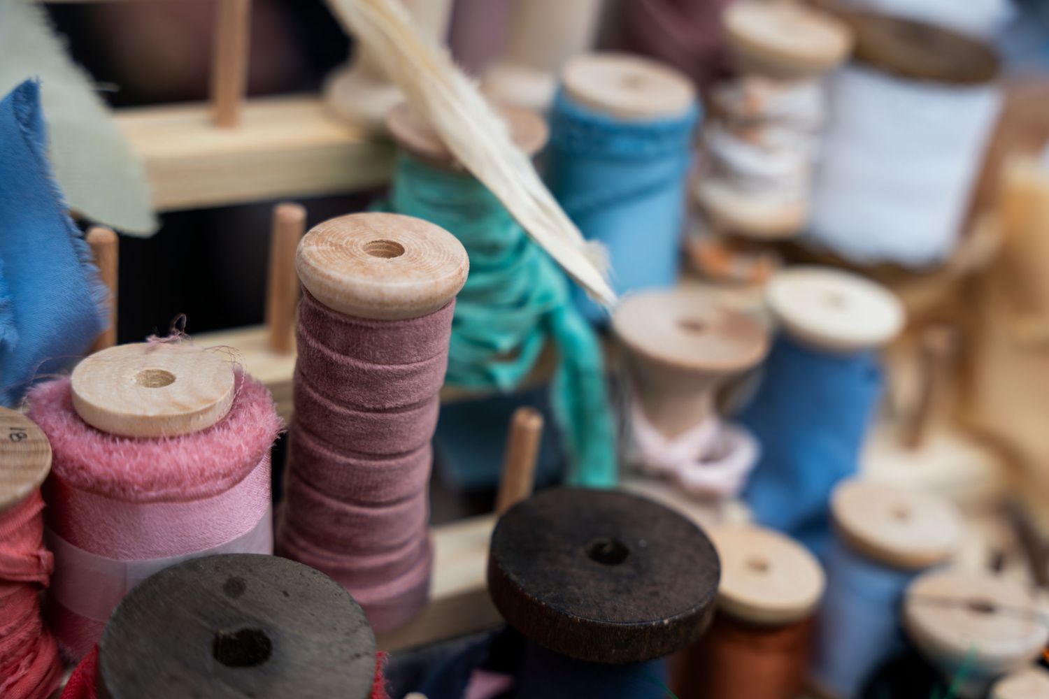 Vintage wooden spools of colorful thread lined up in a row showing varying shades of pink, blue, and neutral tones.