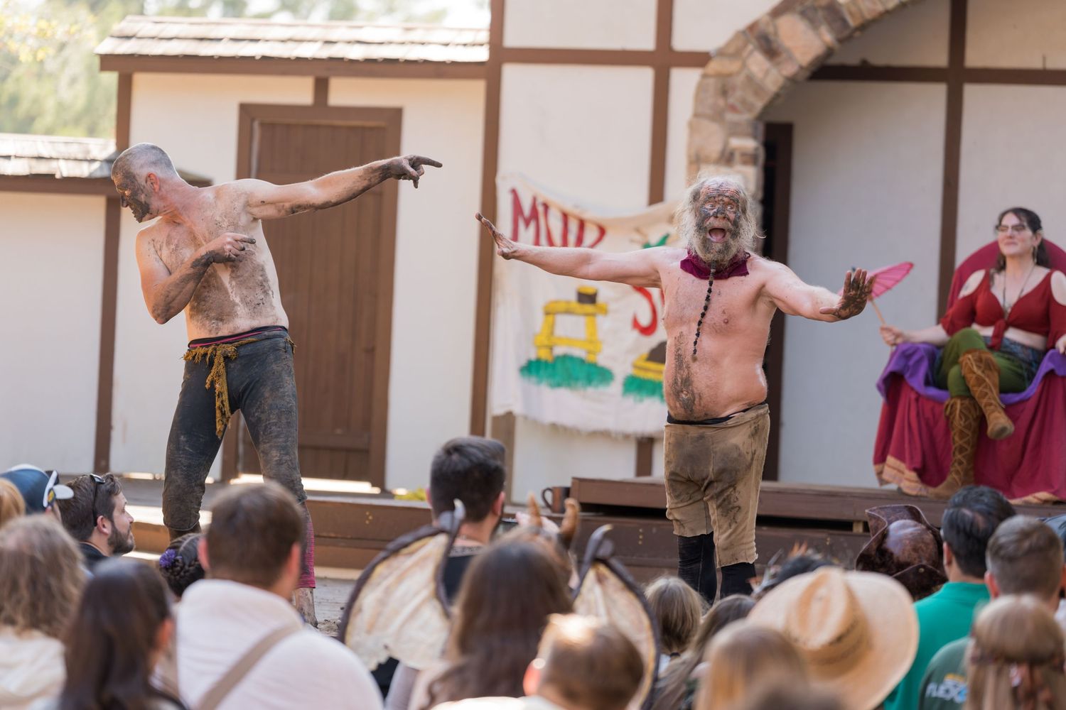 Performers entertain a seated crowd at an outdoor Renaissance festival show.