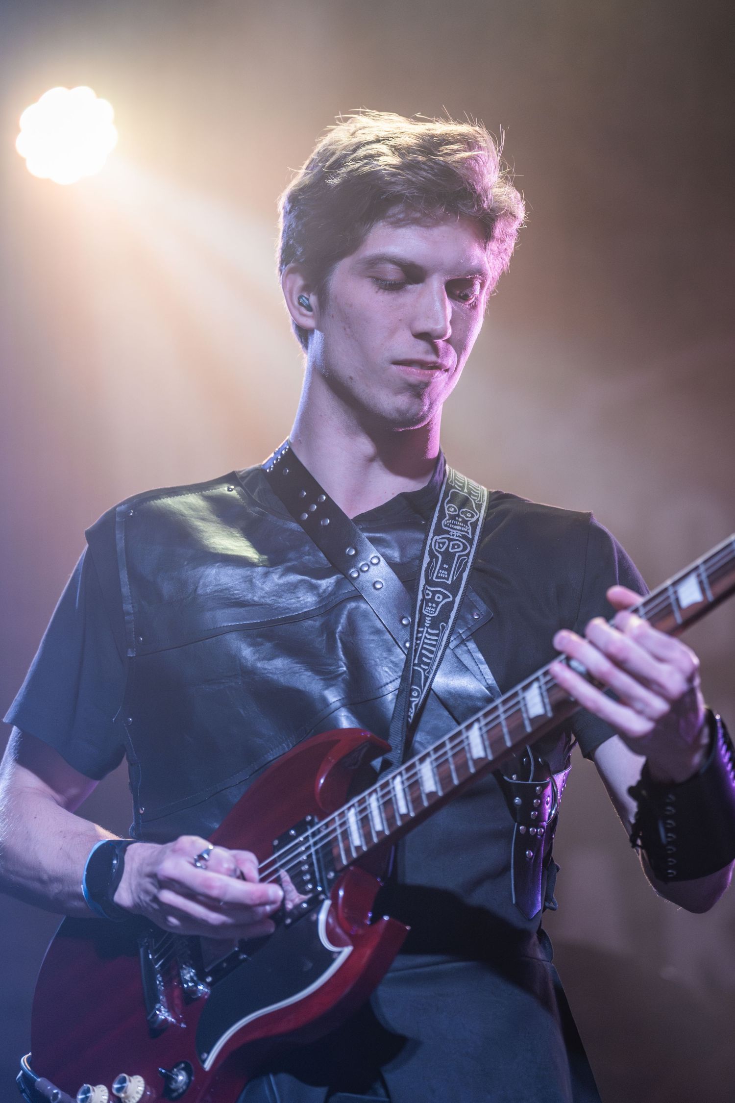 Guitarist focused on playing red electric guitar under dramatic spotlight.