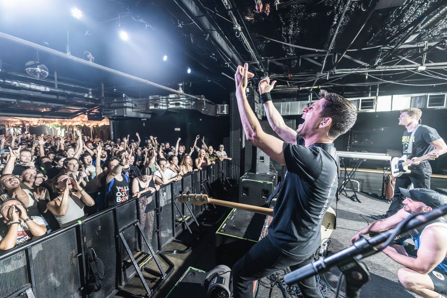 Performer engages with packed crowd from elevated stage position at indoor concert venue.