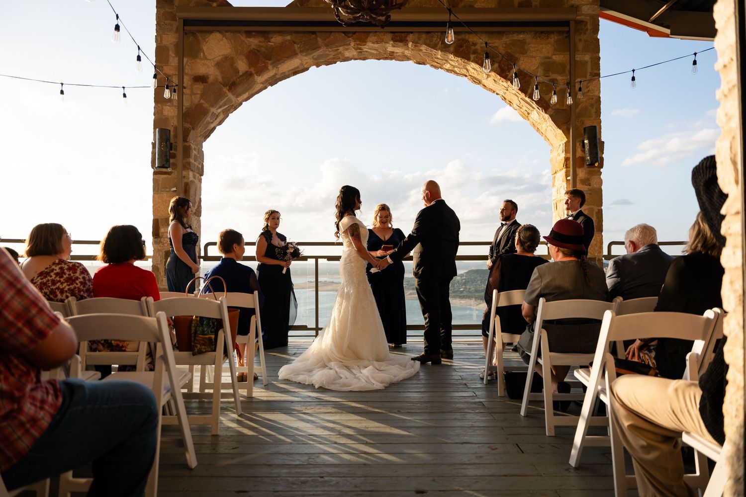 Outdoor wedding ceremony under stone archway with white chairs and ocean backdrop.