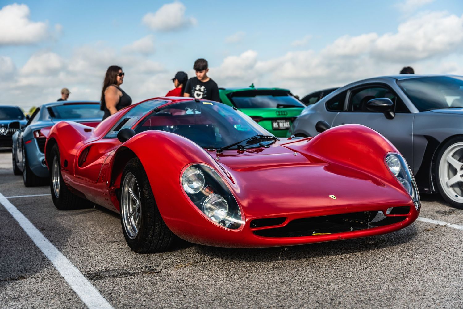 Bright red classic Ferrari sports car with curved bodywork on display at an outdoor car show.