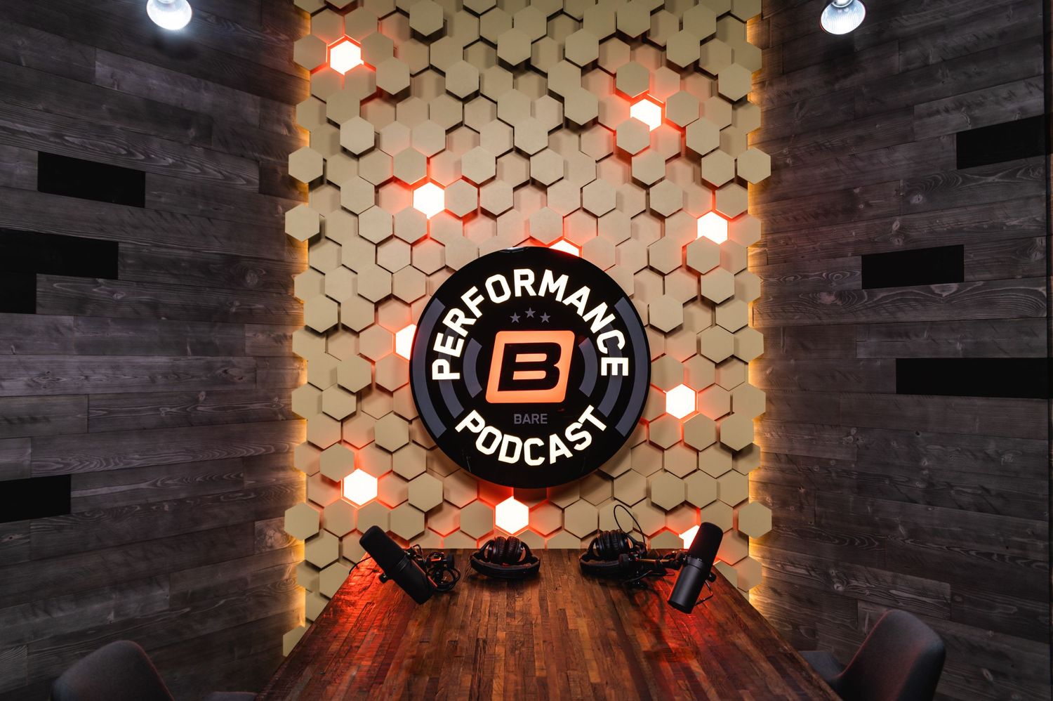 Modern podcast studio interior with hexagonal wall panels and illuminated Performance B Podcast logo sign.