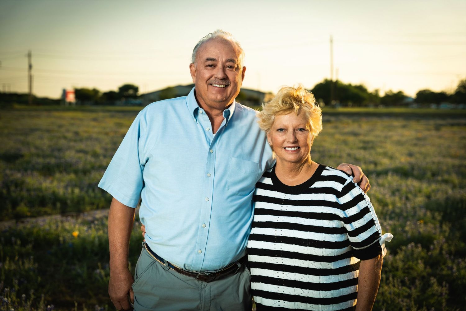 Elderly couple poses together at sunset in rural field setting.