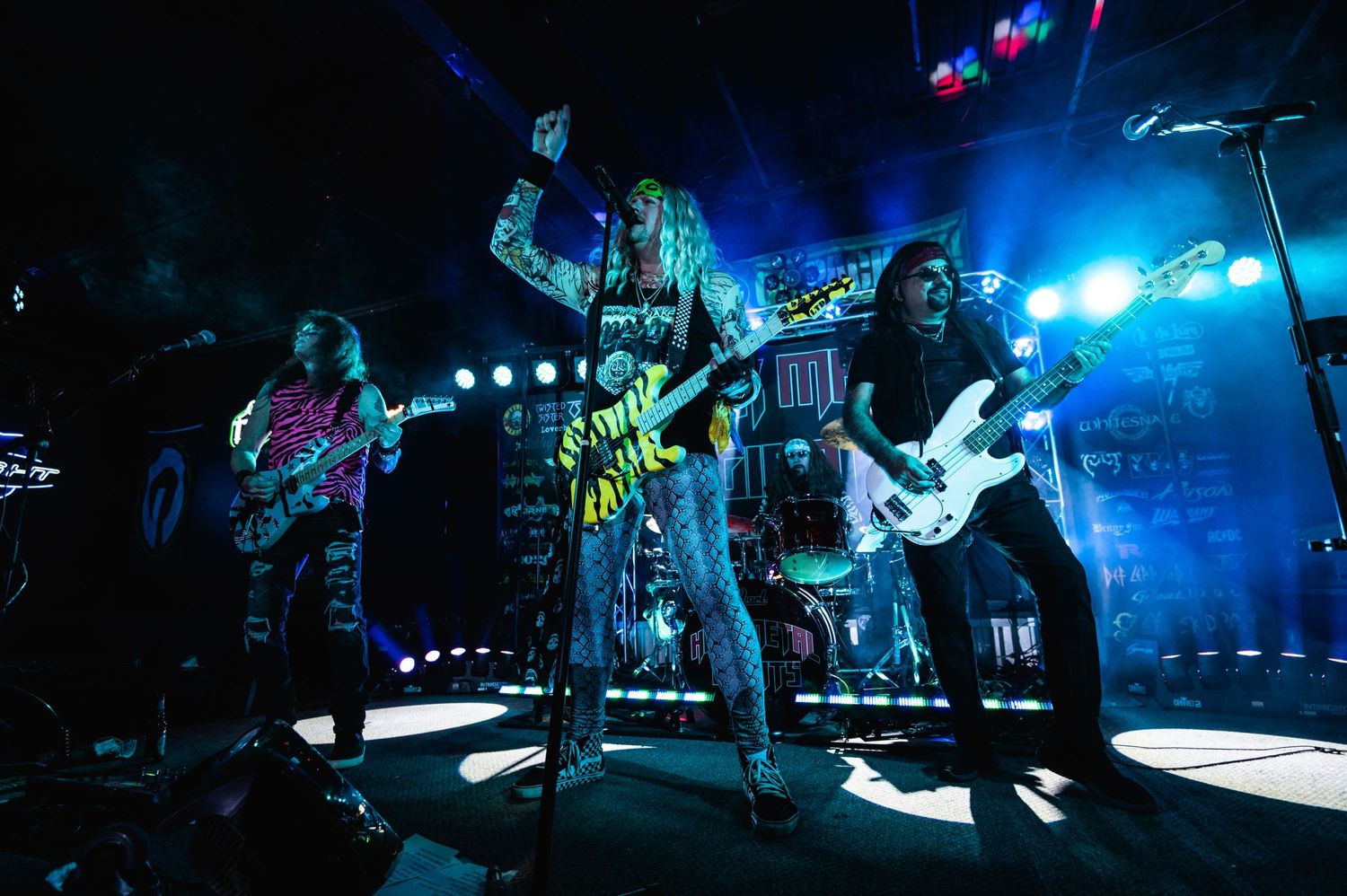 Rock musicians performing energetically under blue stage lights.