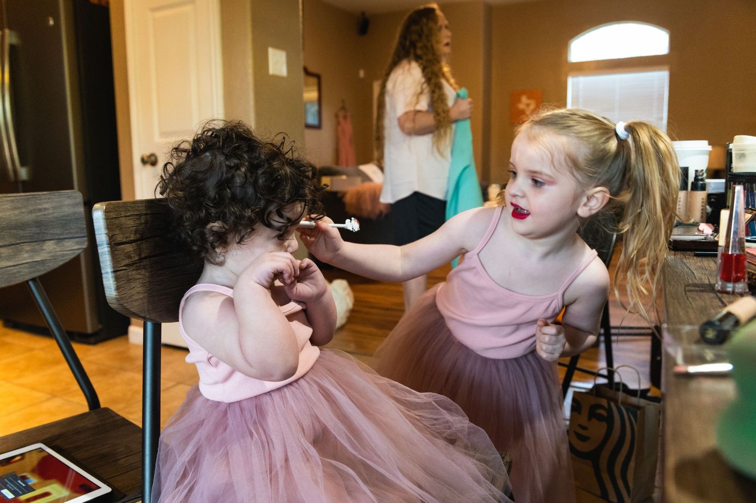 Two young children in pink tutus laughing and playing together indoors.