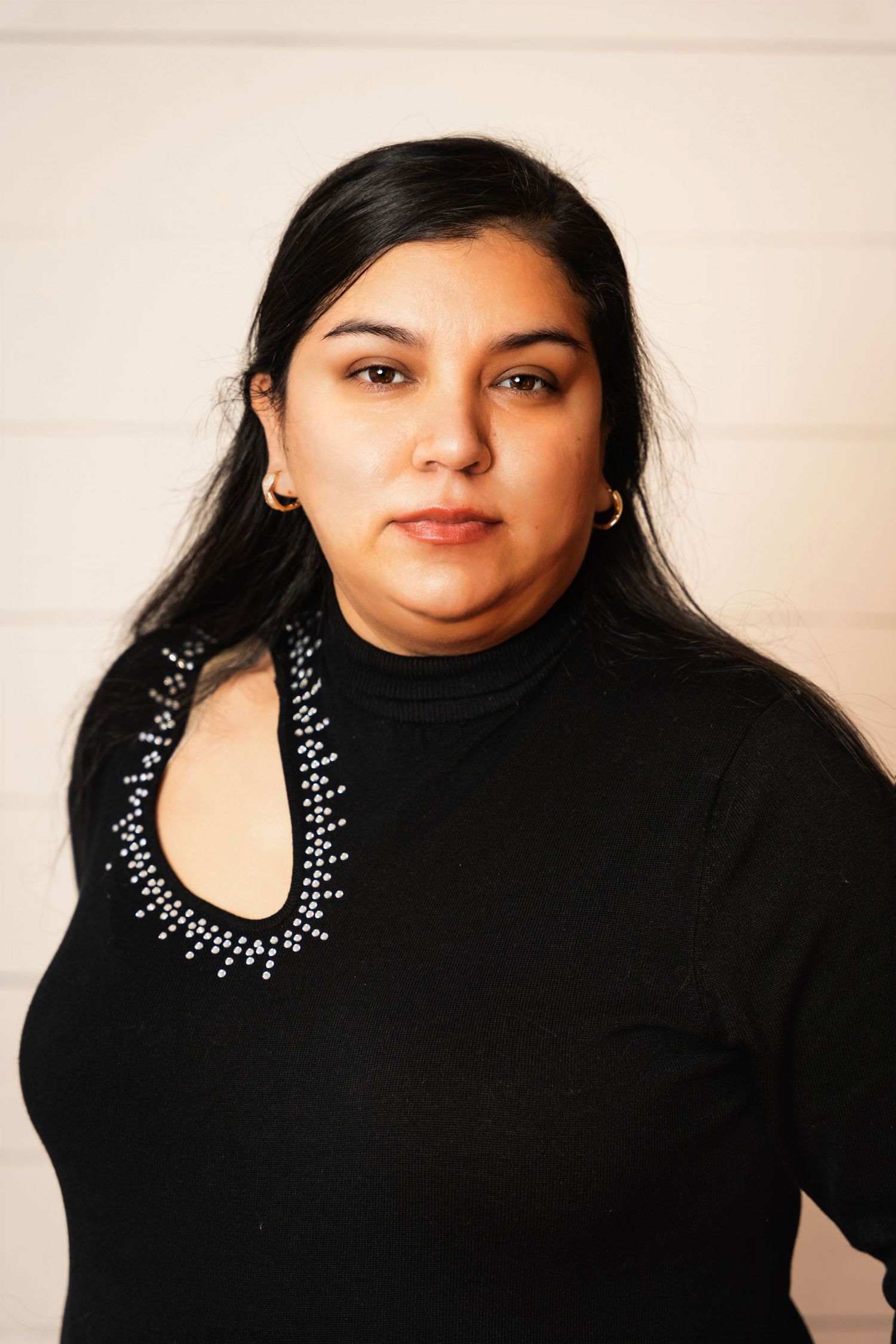 Portrait of person in black top with statement necklace against light background.