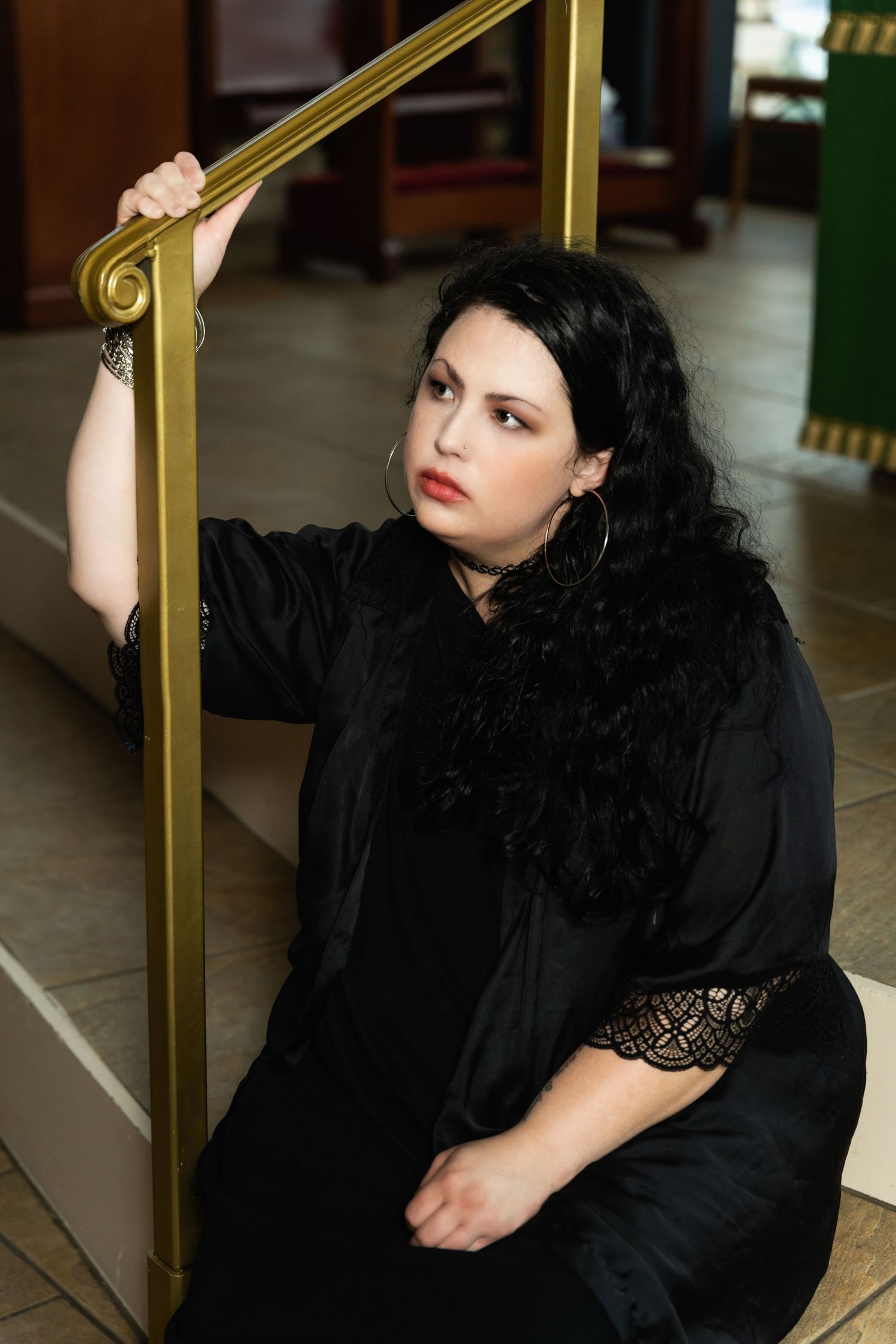 Person in black clothing seated by gold handrail in church interior with dramatic lighting.