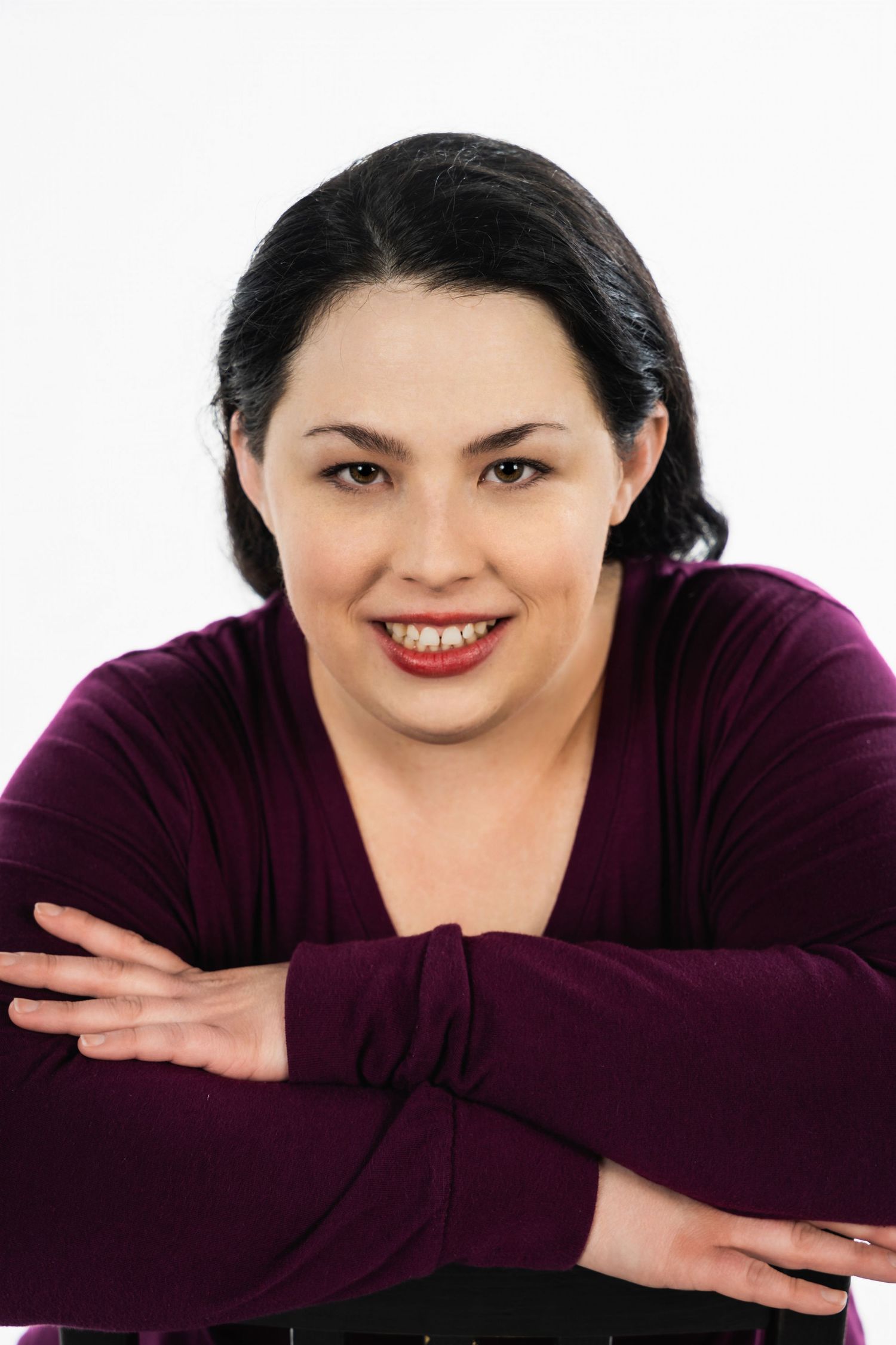 Portrait of a woman in burgundy sweater resting chin on crossed arms against white background.