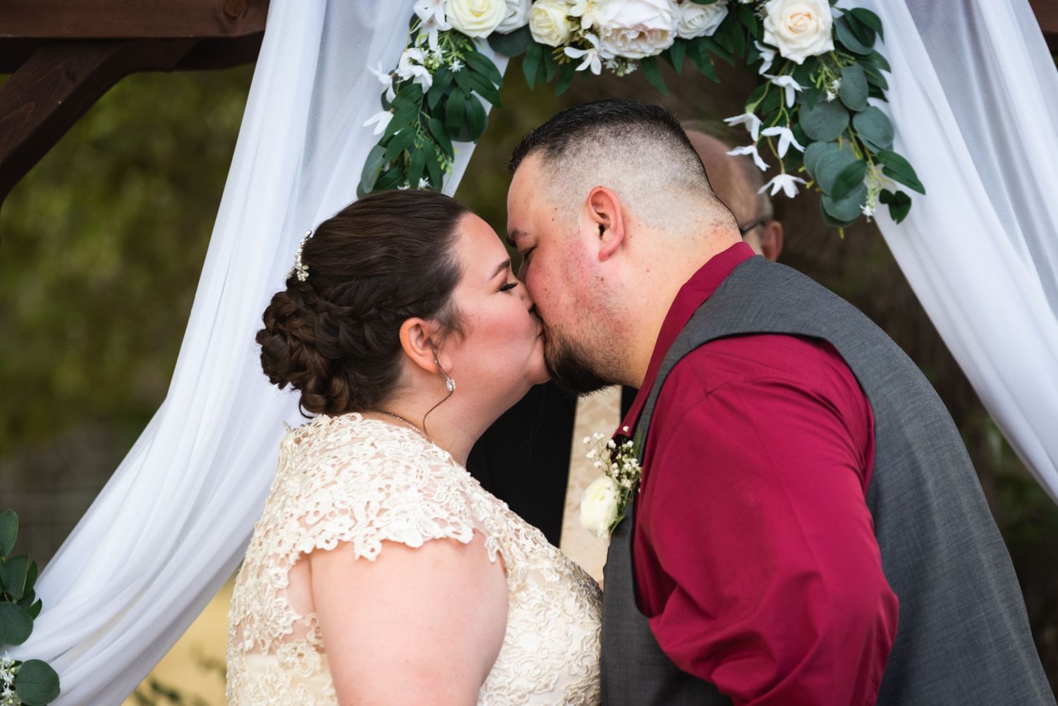 Romantic kiss shared under floral-decorated wedding arch during outdoor ceremony.