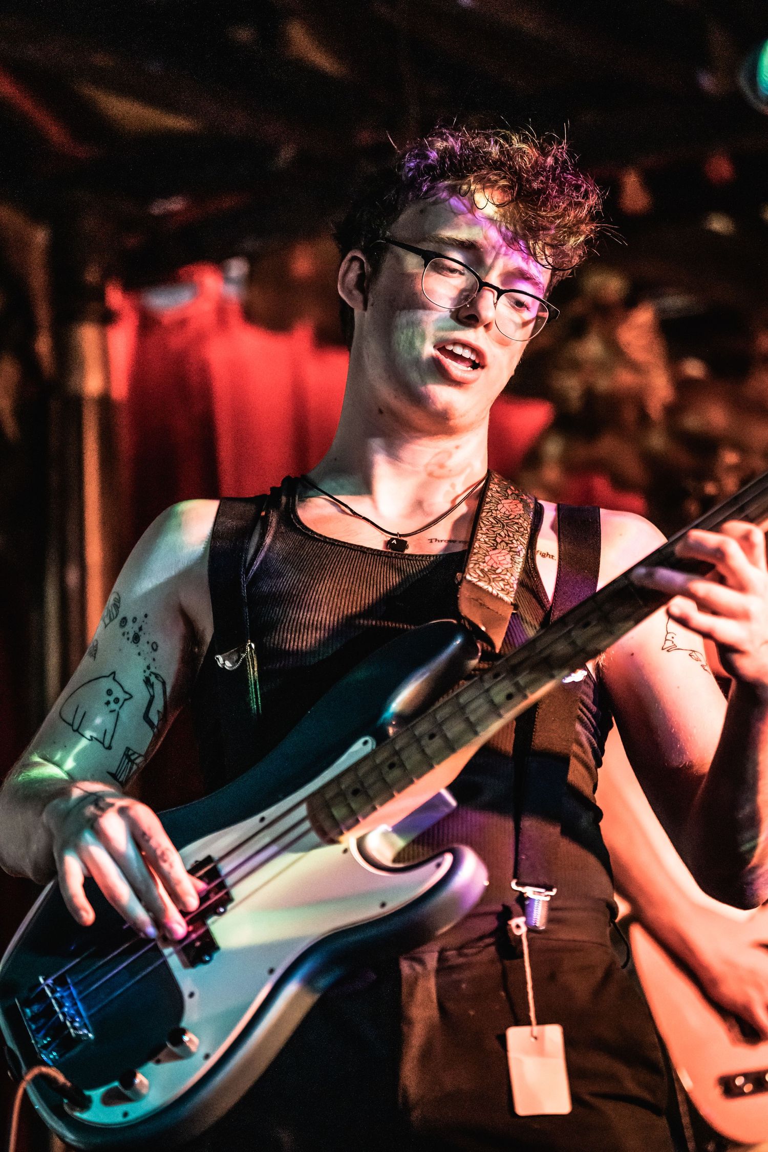 A musician plays bass guitar on stage under dramatic purple and red lighting.