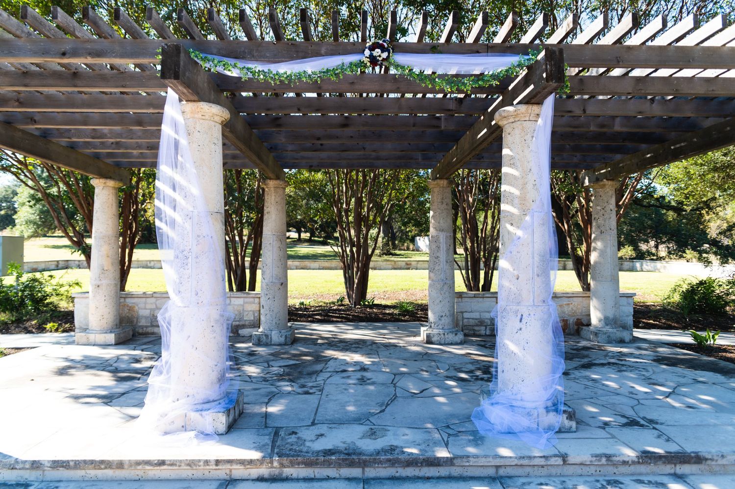 White drapes hanging from outdoor pergola structure with stone columns.