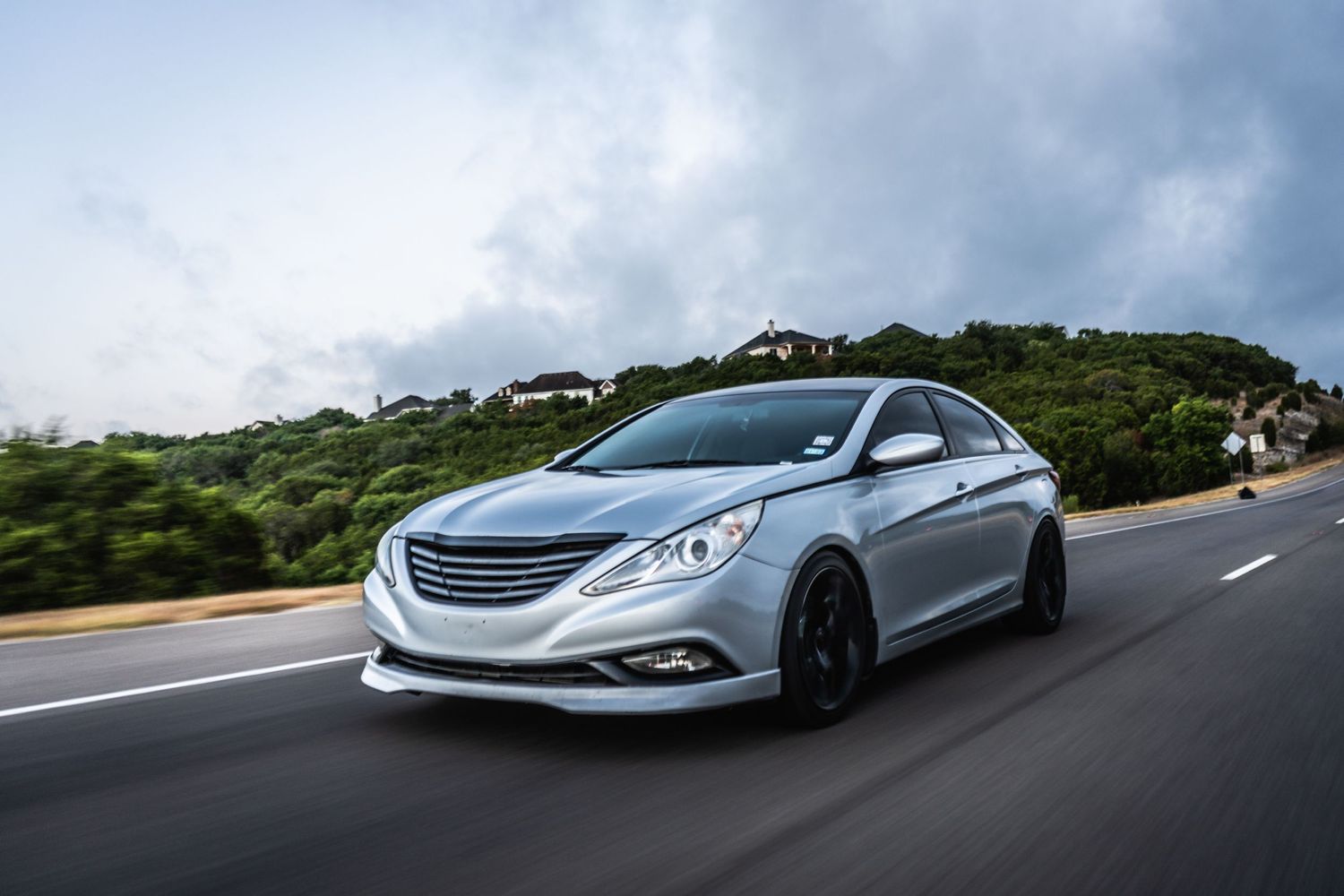 Silver Hyundai Sonata sedan with custom black wheels driving on a coastal highway.