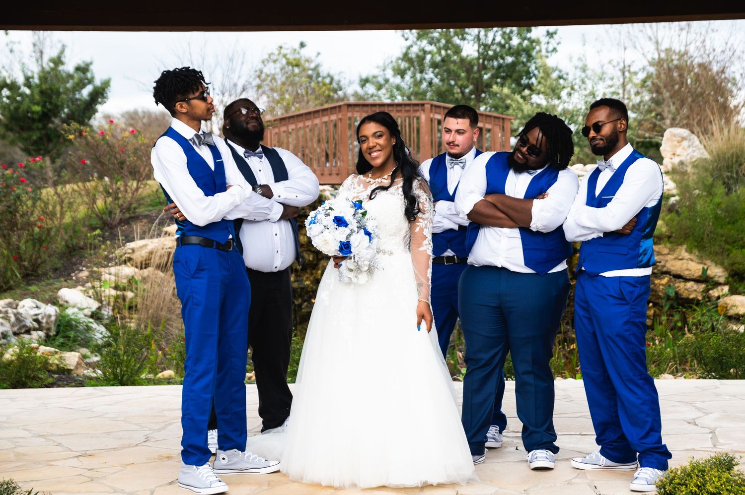 Wedding party poses together outdoors wearing coordinated blue and white attire with bouquets.