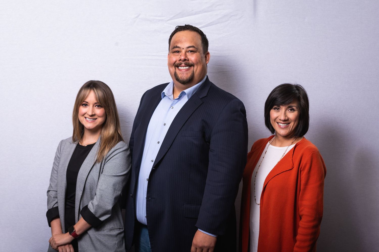 Group professional photo of three people in business attire against a gray studio background.