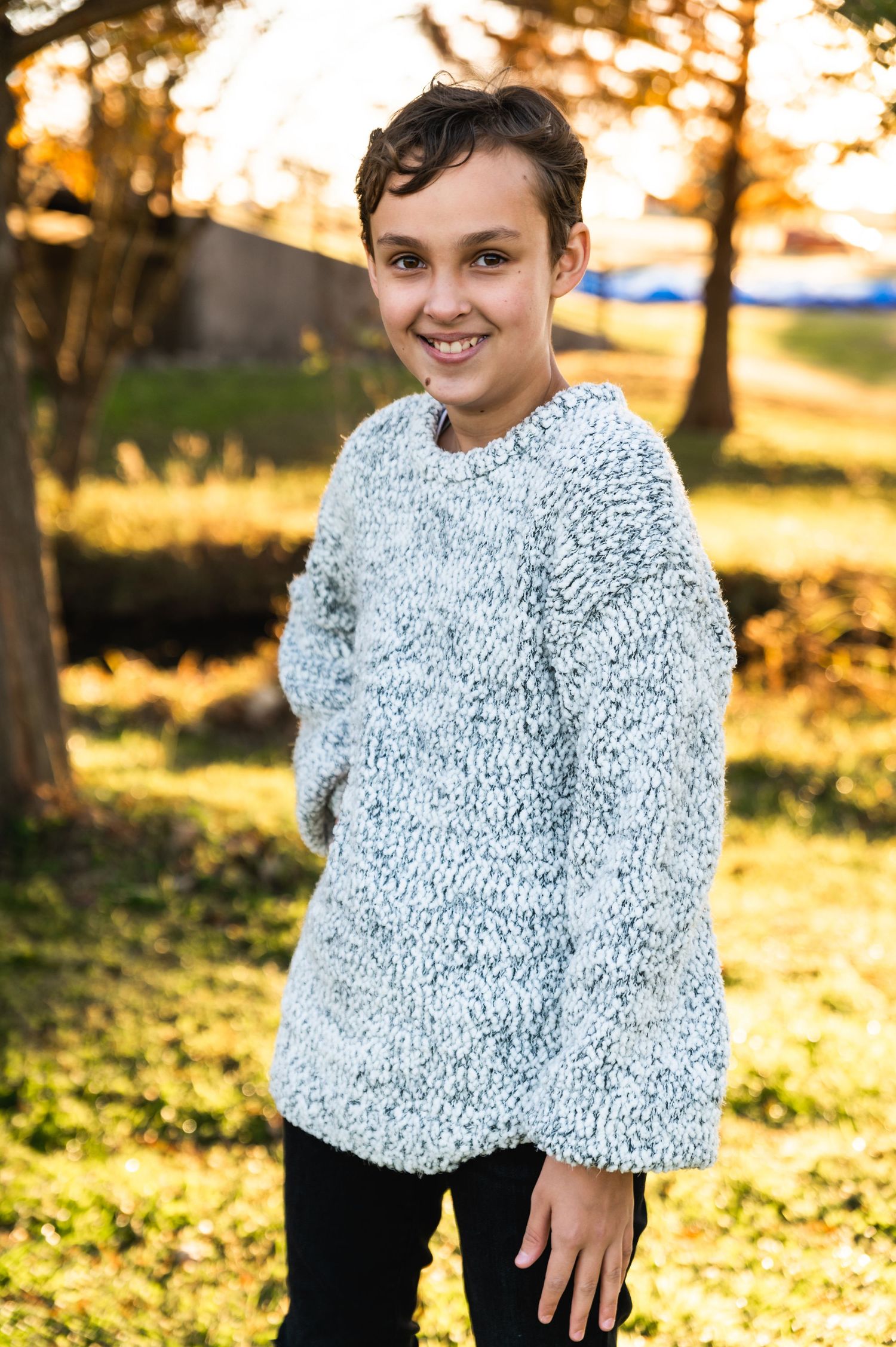 Portrait of someone in a cozy knit sweater during sunset with fall foliage in background.