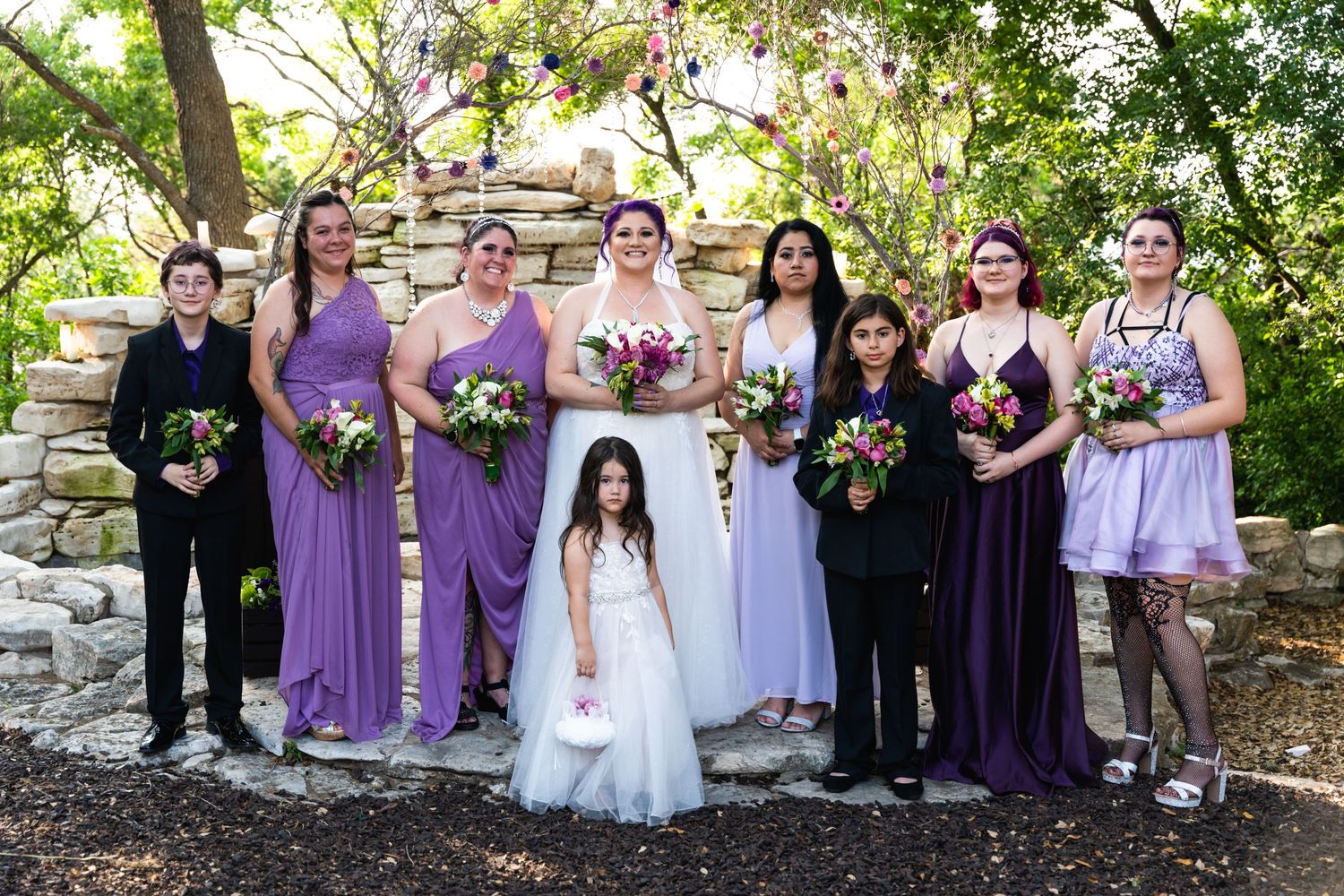 Wedding party in purple and black attire poses for formal photo on stone steps.