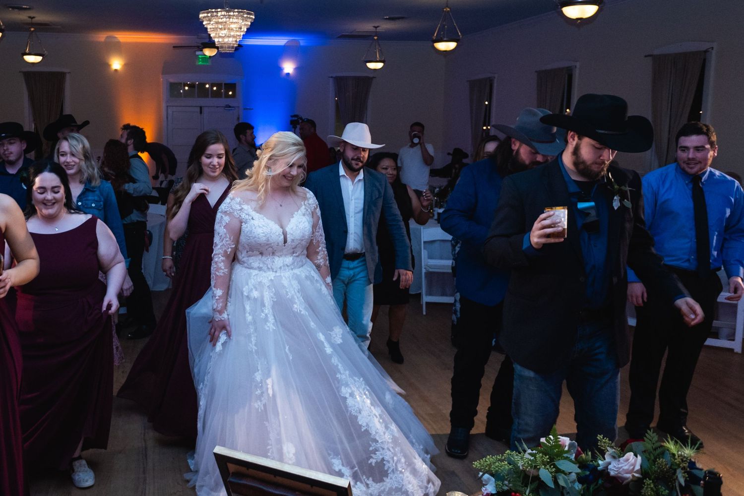 Wedding guests dancing and celebrating at a reception with blue and orange lighting.