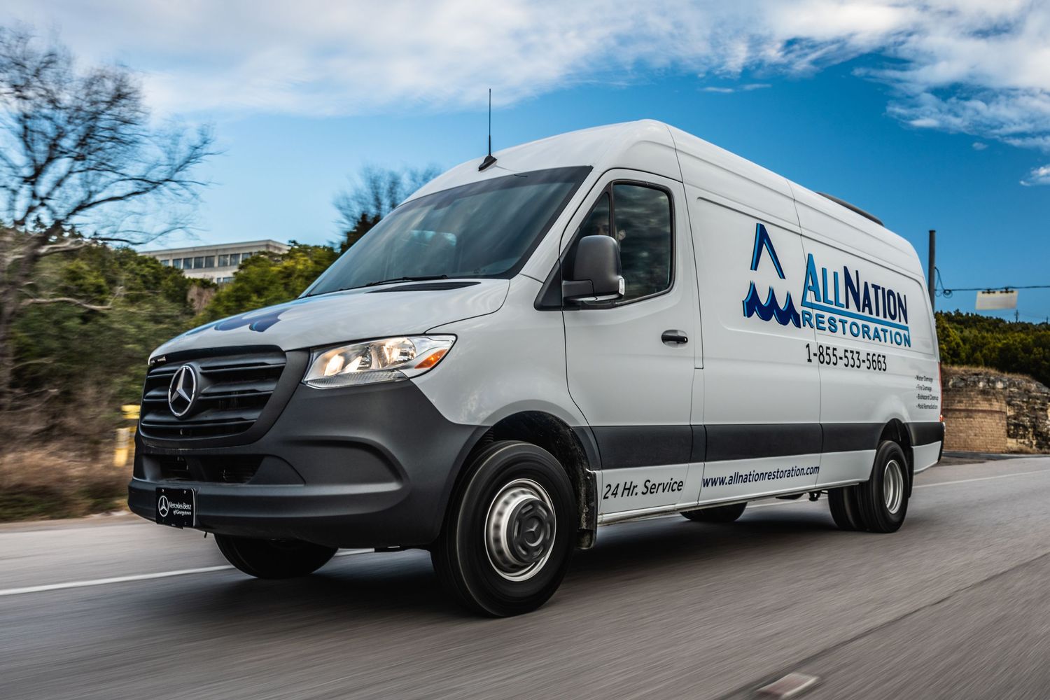 All North white Mercedes Sprinter van driving on a road against blue sky.