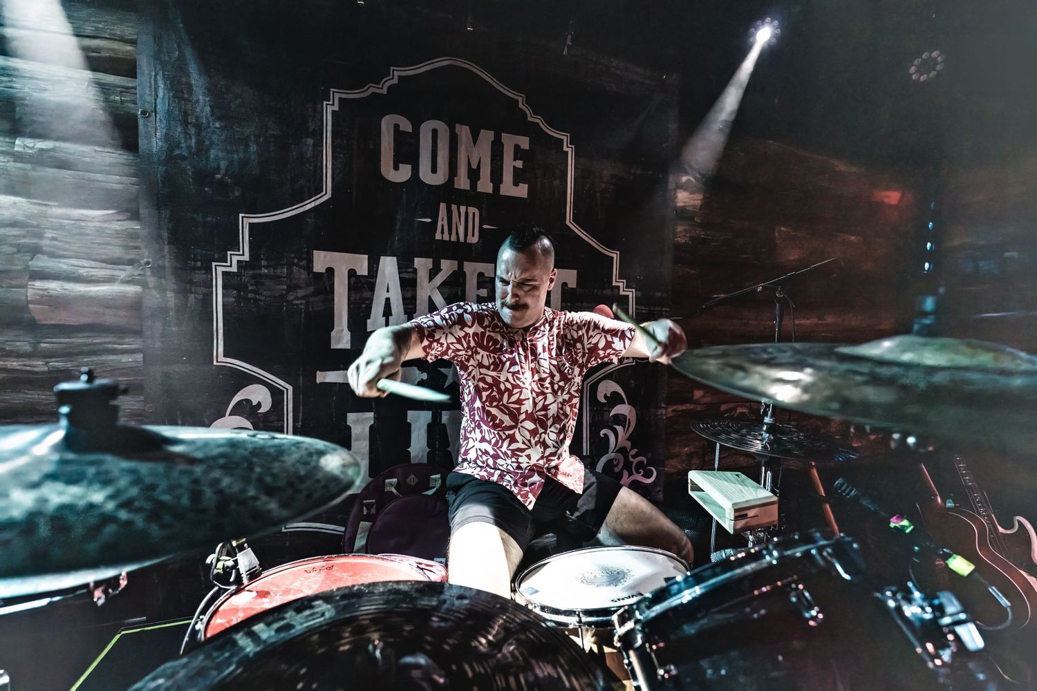 Drummer performs on stage with 'Come and Take It' signage and dramatic lighting.