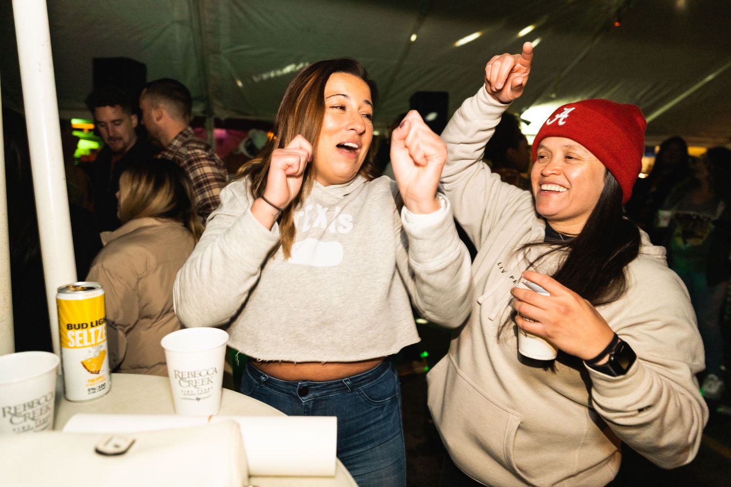 Two friends enjoying a lively night out with dancing and drinks under colorful party lights.