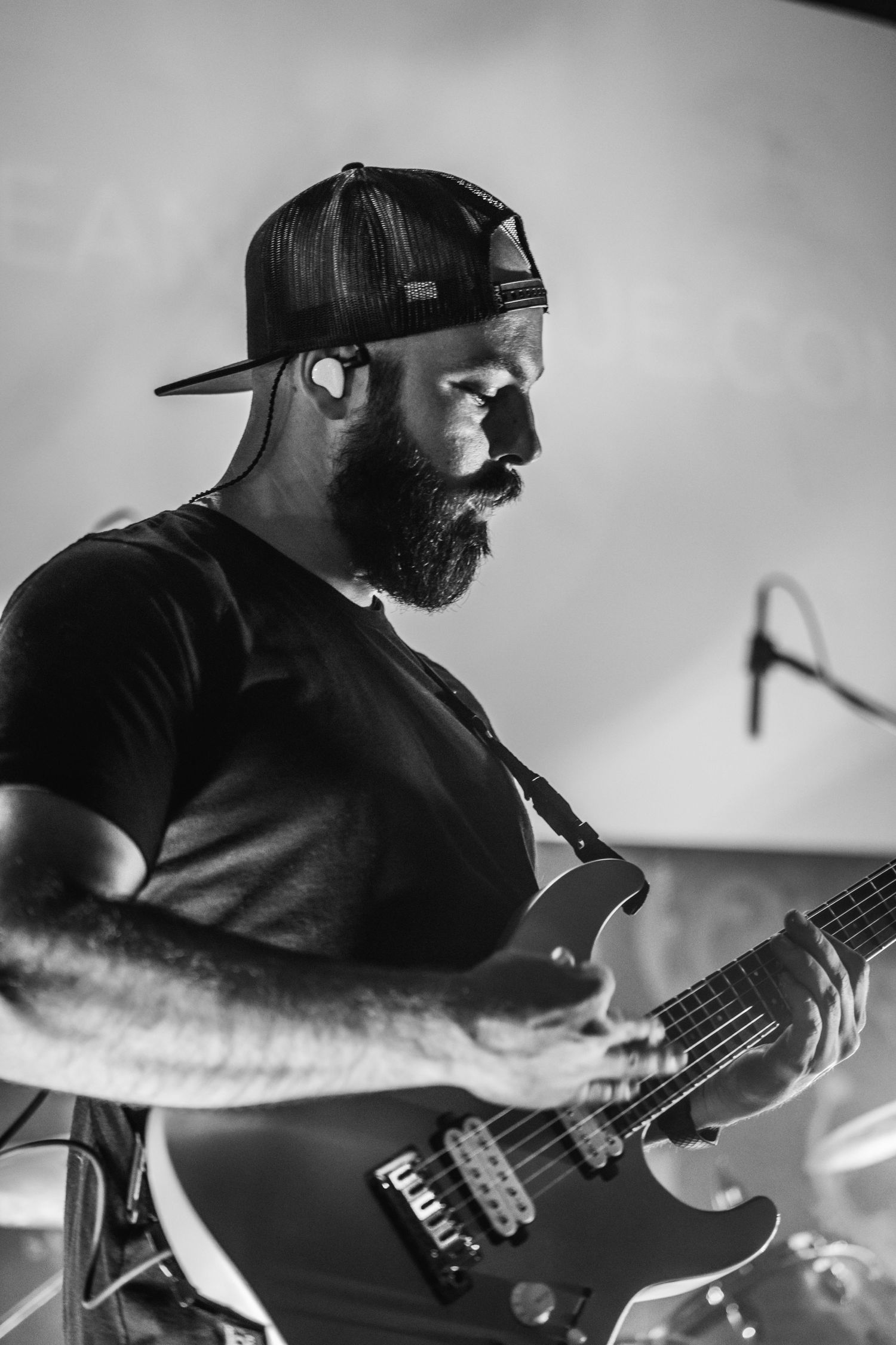 Monochrome portrait of musician with beard wearing baseball cap while playing guitar.