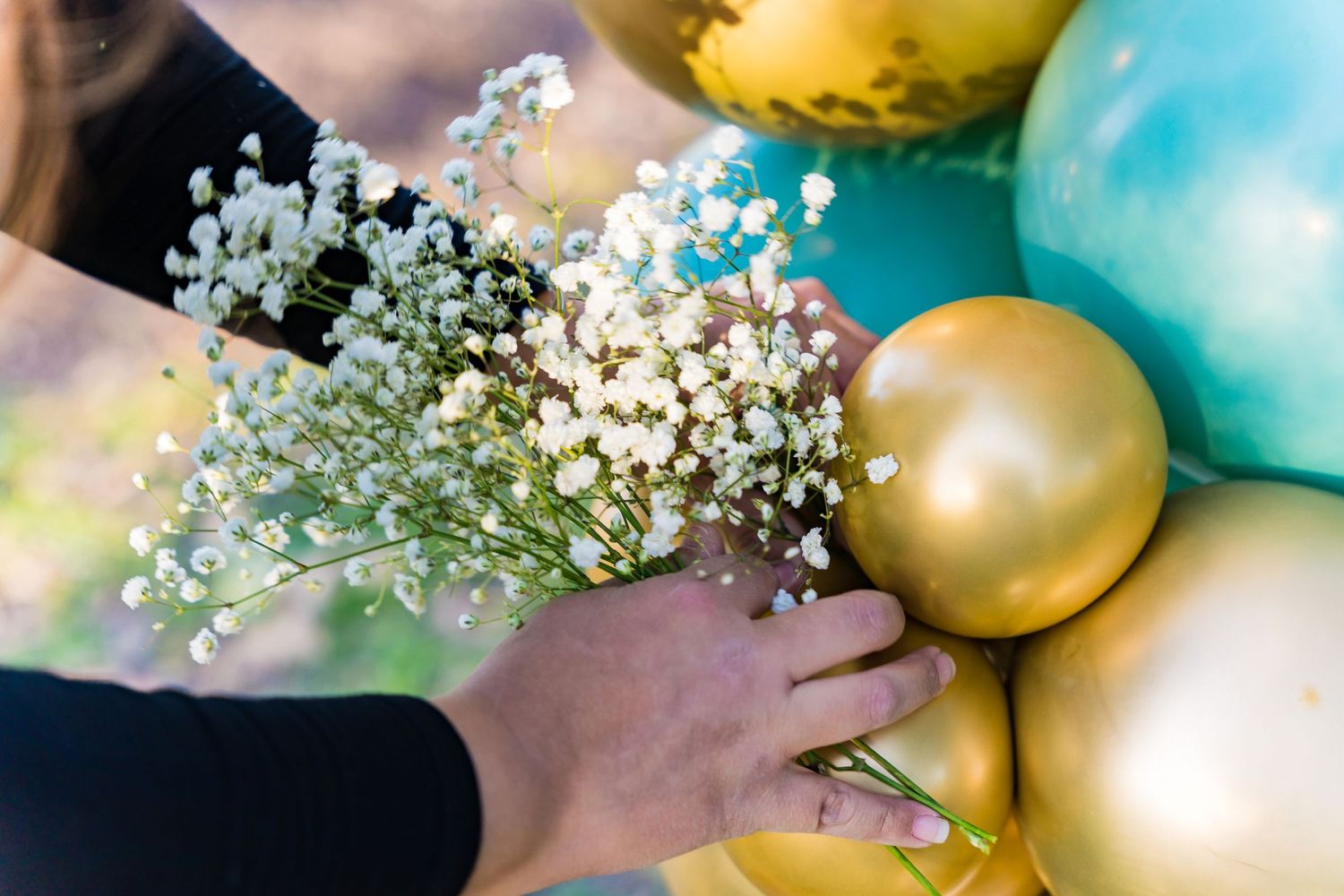 Delicate baby's breath flowers accent a balloon display with gold and teal spheres.